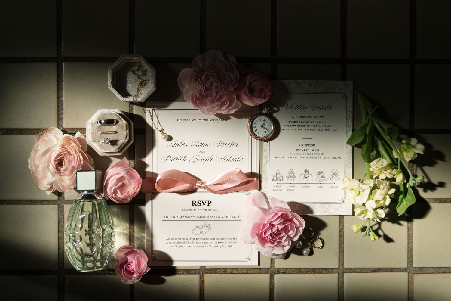 A romantic wedding flat lay with pink ranunculus, RSVP cards, a vintage watch, and perfume on tiles.