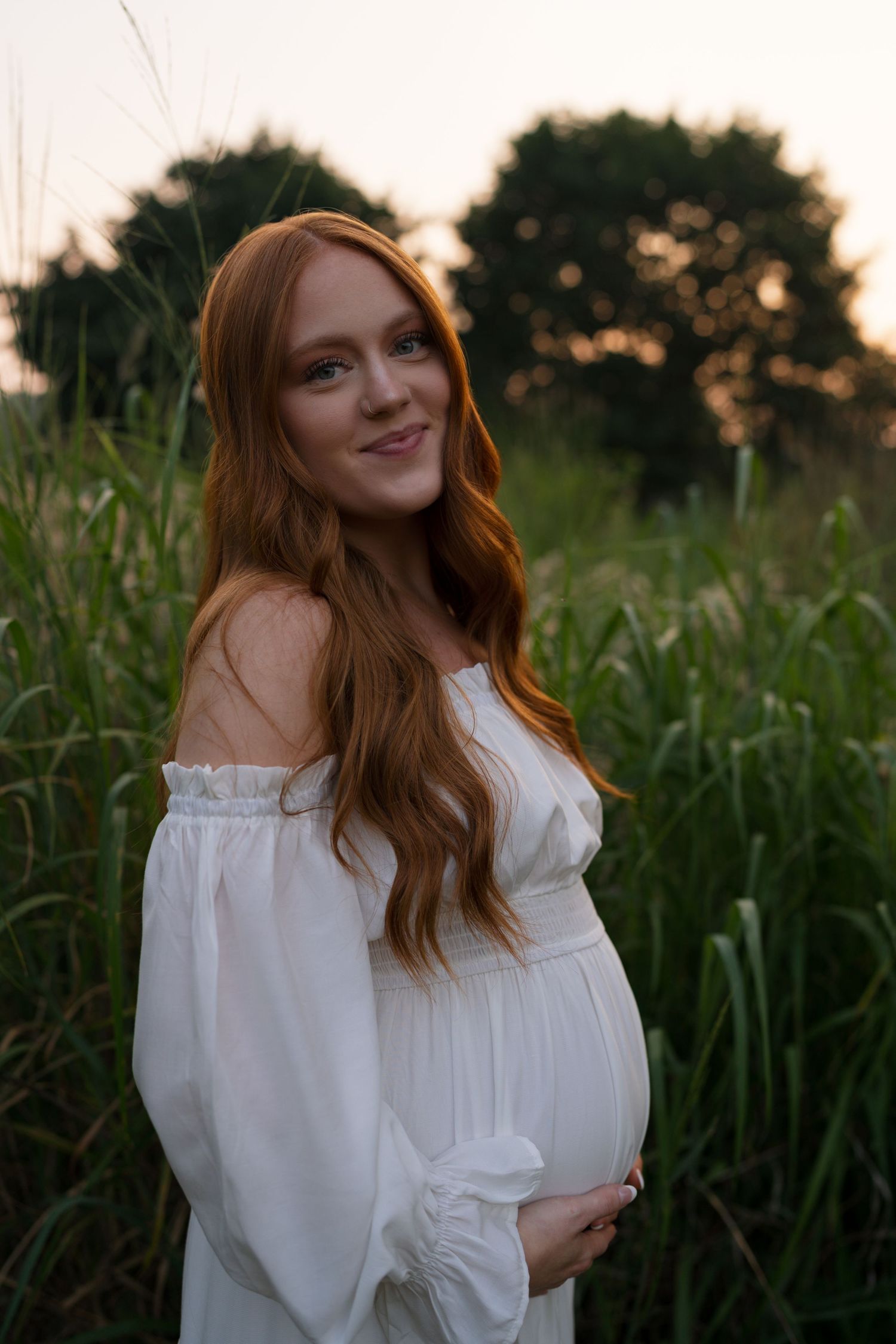 Expectant parents standing together in the prairie during golden hour.