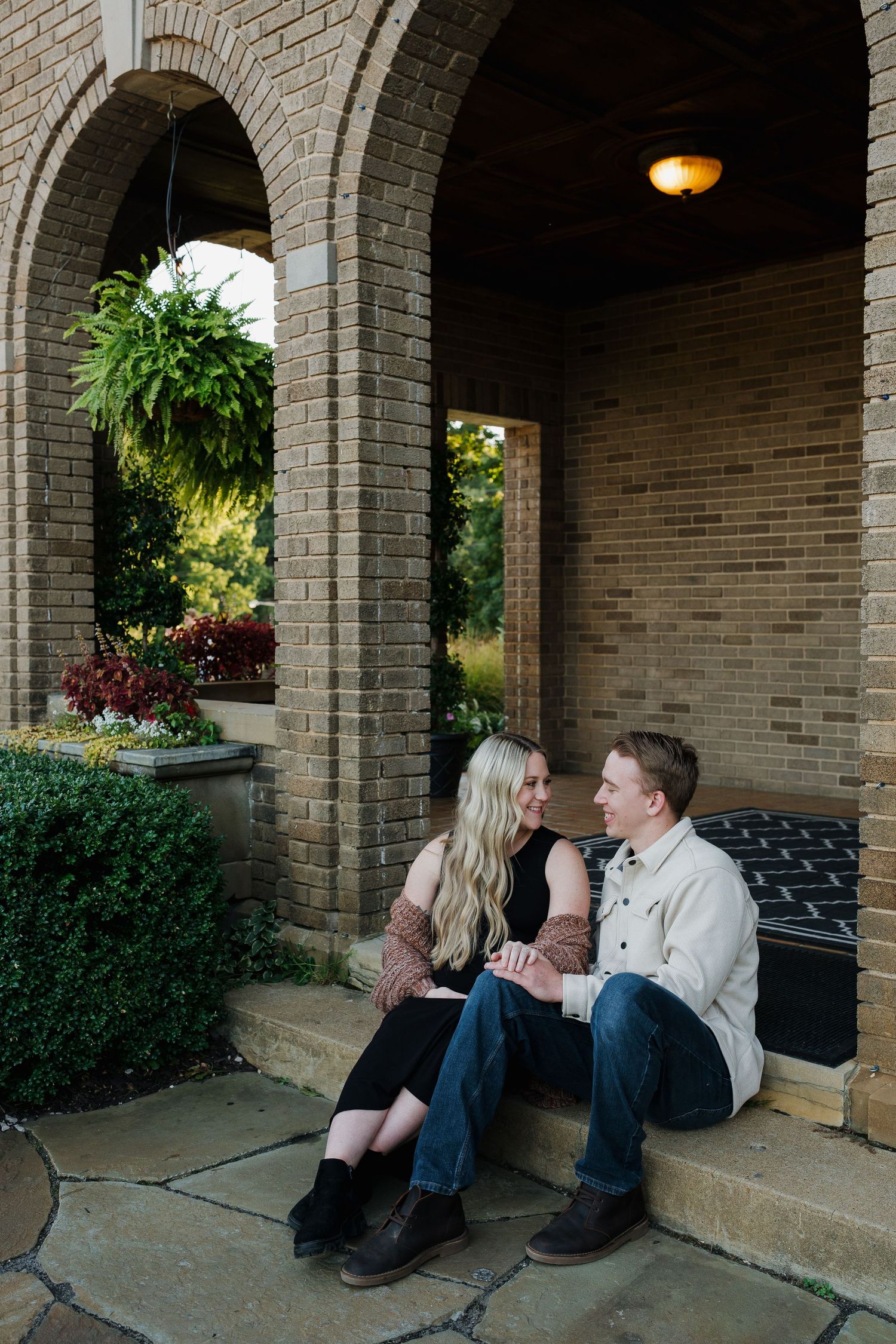 Happy couple sitting together on stone steps under elegant brick arches in a garden setting.