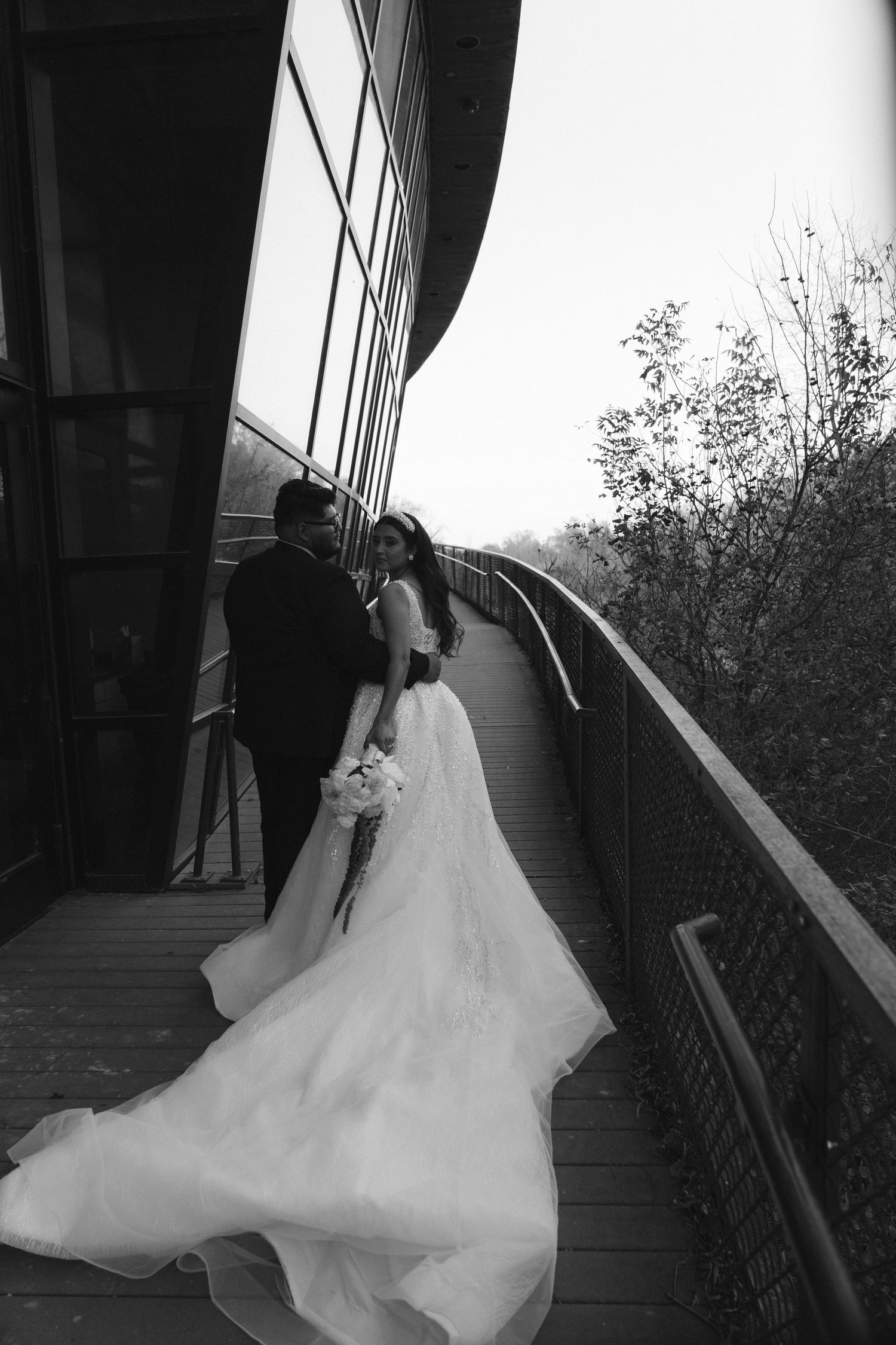 Black and white photo of a bride and groom on a wooden walkway with a flowing wedding gown.
