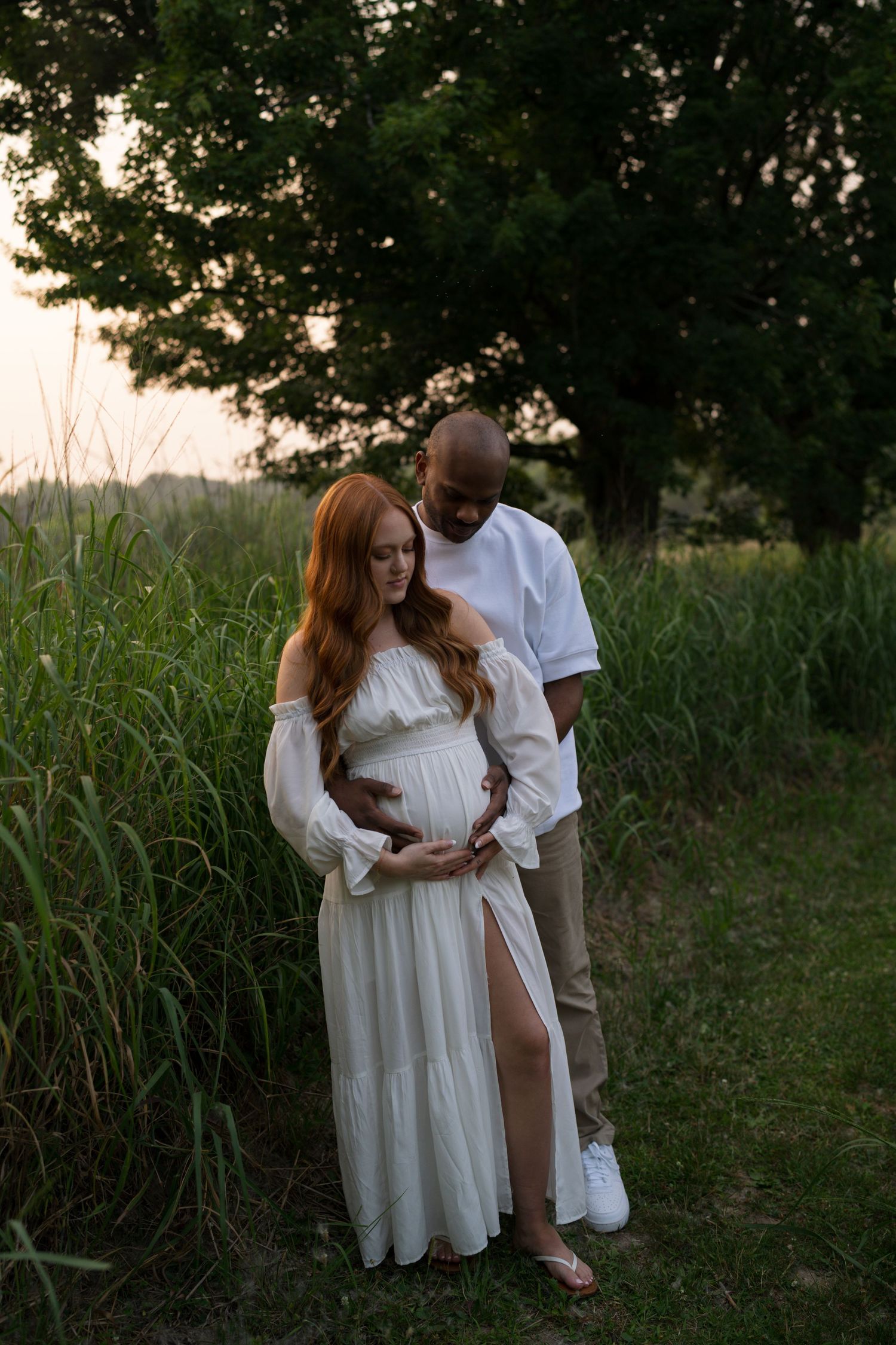 Expectant parents embracing in the tall grasses at Highlands Prairie.