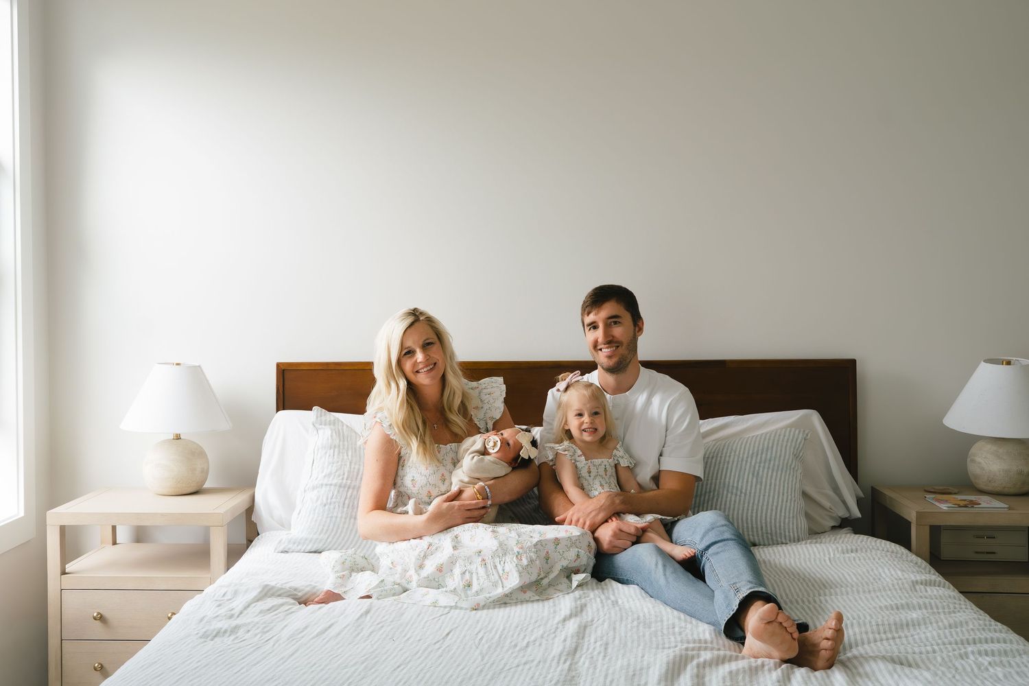 Young family cuddling together with their newborn in a bright bedroom, photographed by Grand Rapids family and wedding photographer Mariah.
