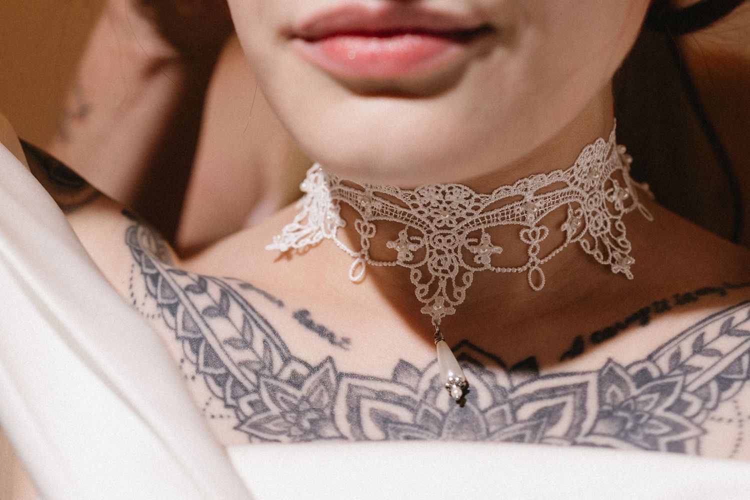 Close-up of a lace choker necklace on a tattooed woman's chest and collarbone area.