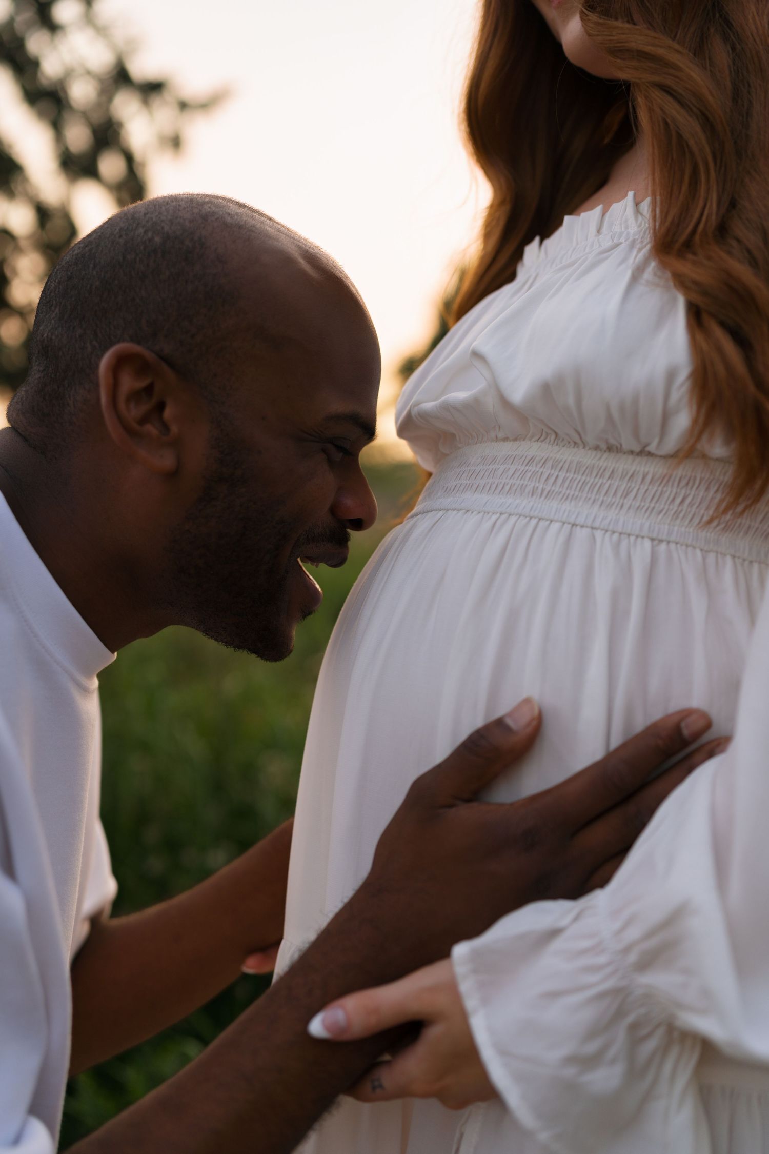 Expectant parents embracing in the tall grasses at Highlands Prairie.