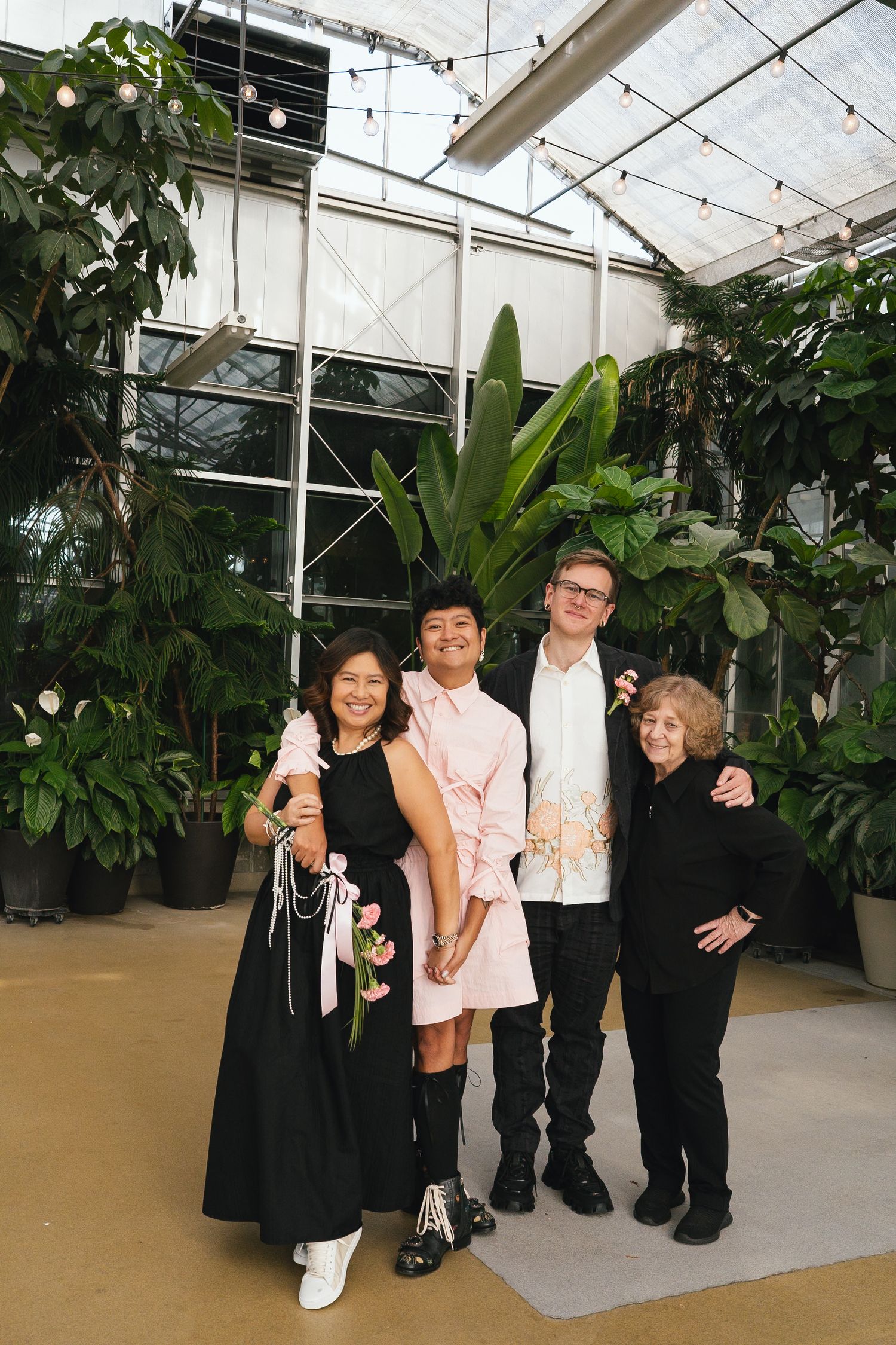 Four people pose together smiling in a lush greenhouse venue during a wedding celebration.