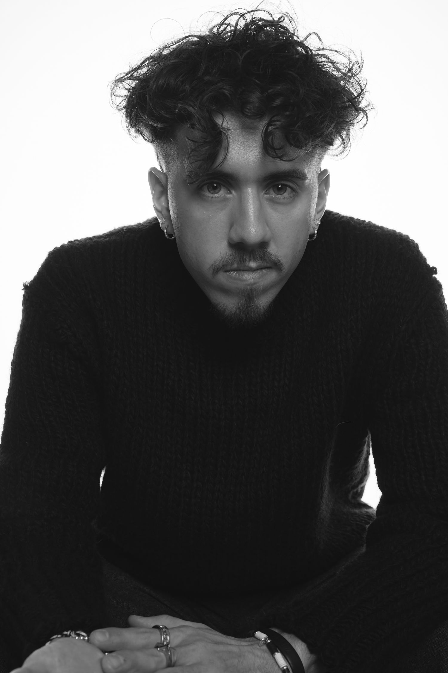 Black and white portrait of curly-haired young man in black sweater gazing directly at camera.