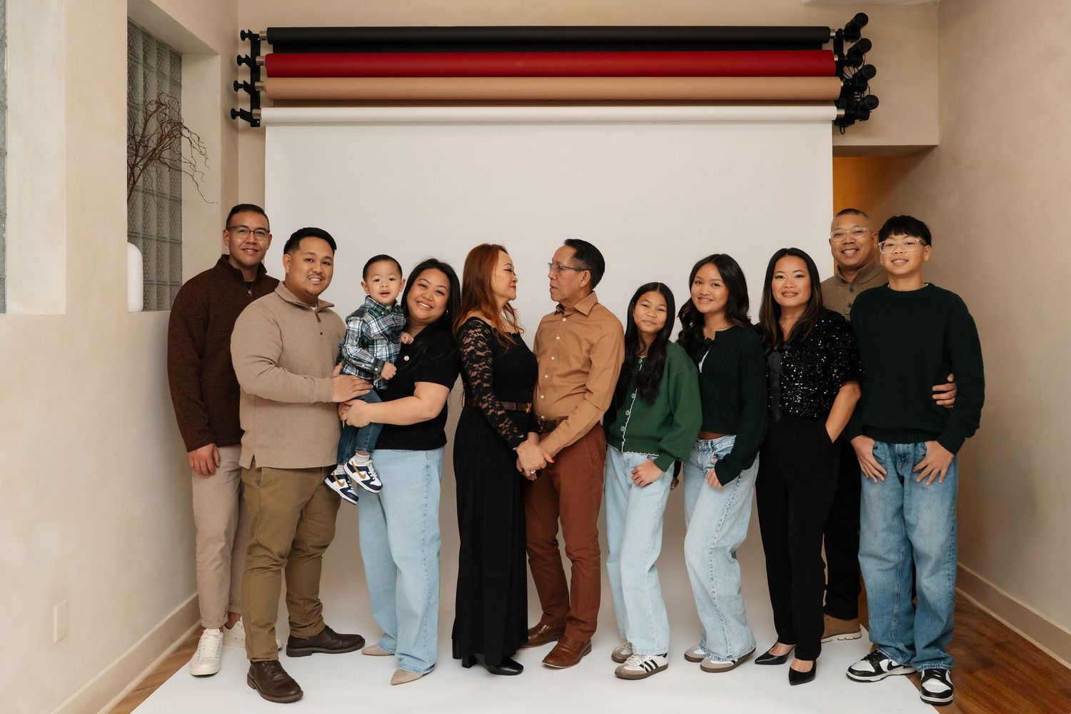 A large diverse family group poses together smiling in front of a white backdrop in a bright modern studio setting.