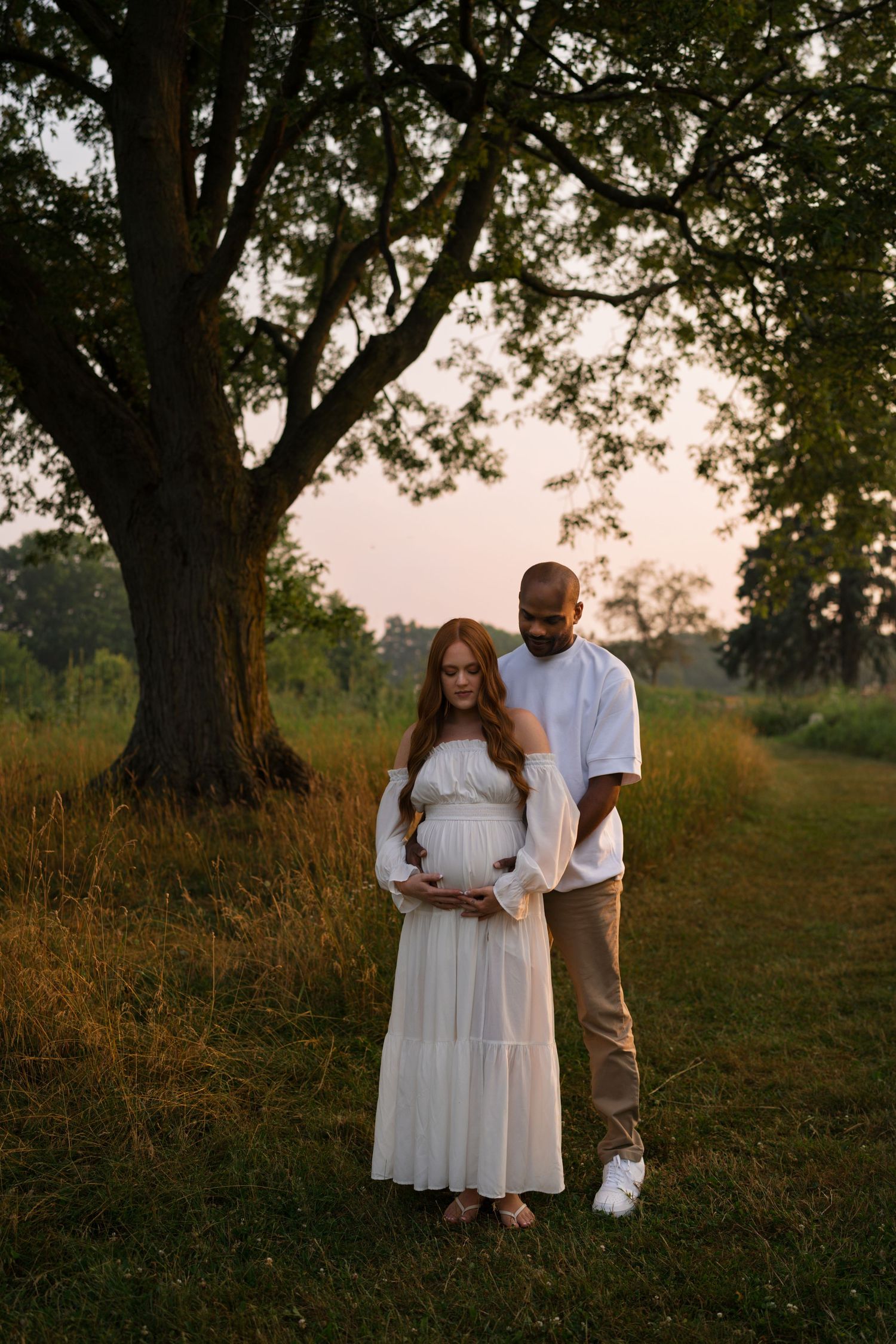 Expectant parents embracing beneath the evening sky at Highlands Prairie.
