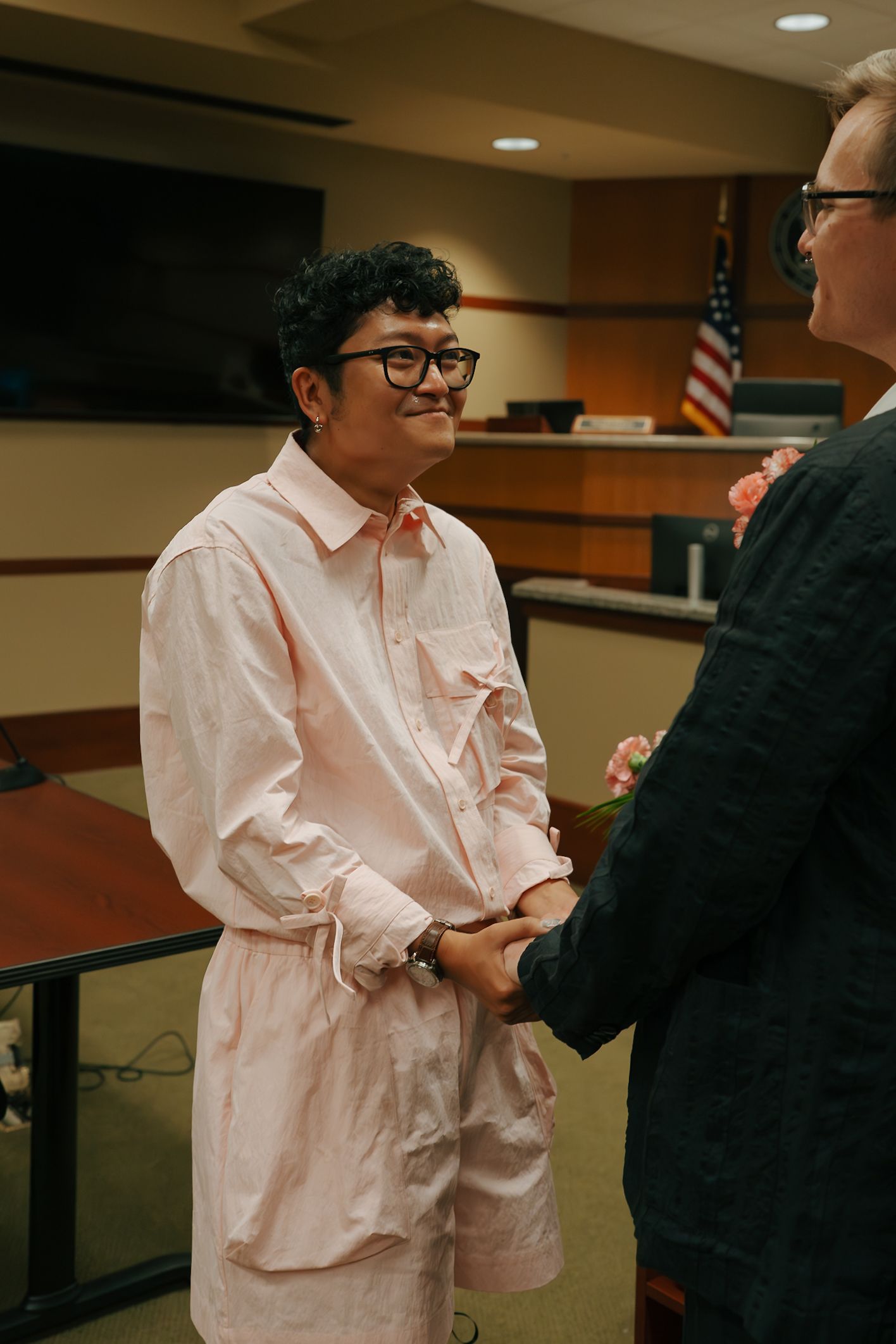 Happy person in pink outfit smiling while holding hands during courthouse wedding ceremony.