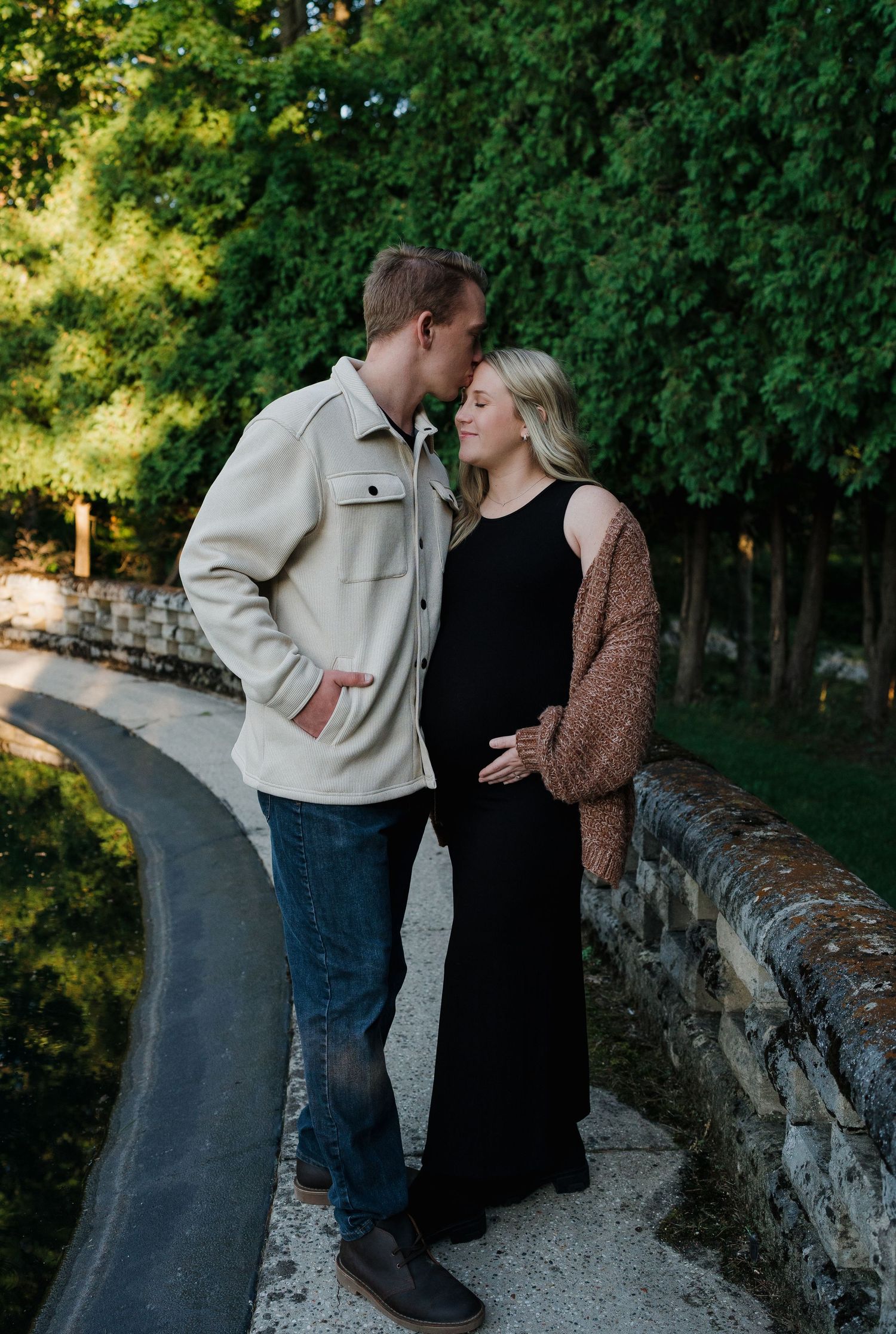 Couple sharing a tender kiss on a stone bridge path surrounded by green foliage.