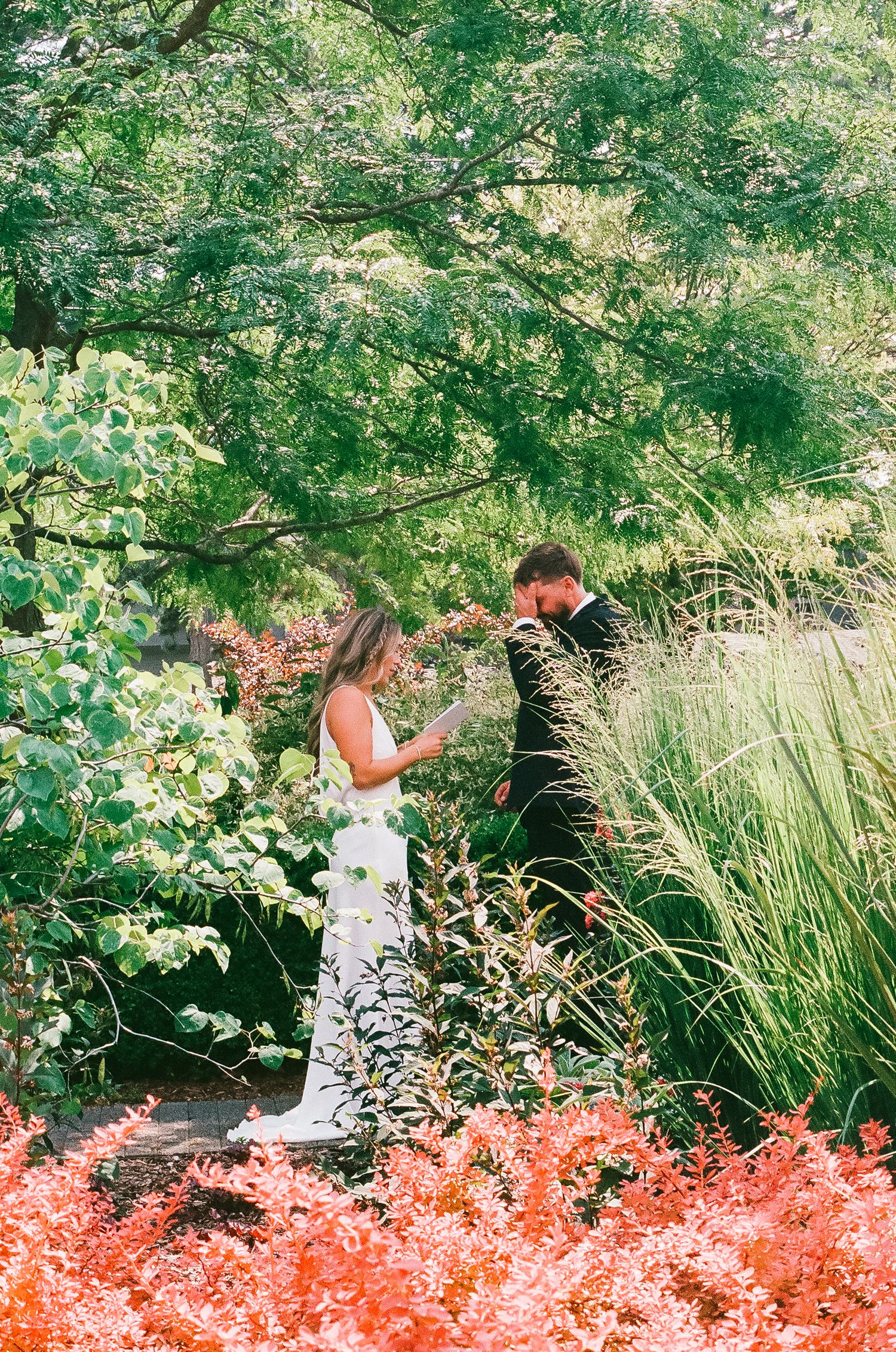 Couple sharing vows in a lush garden surrounded by vibrant red and green foliage.