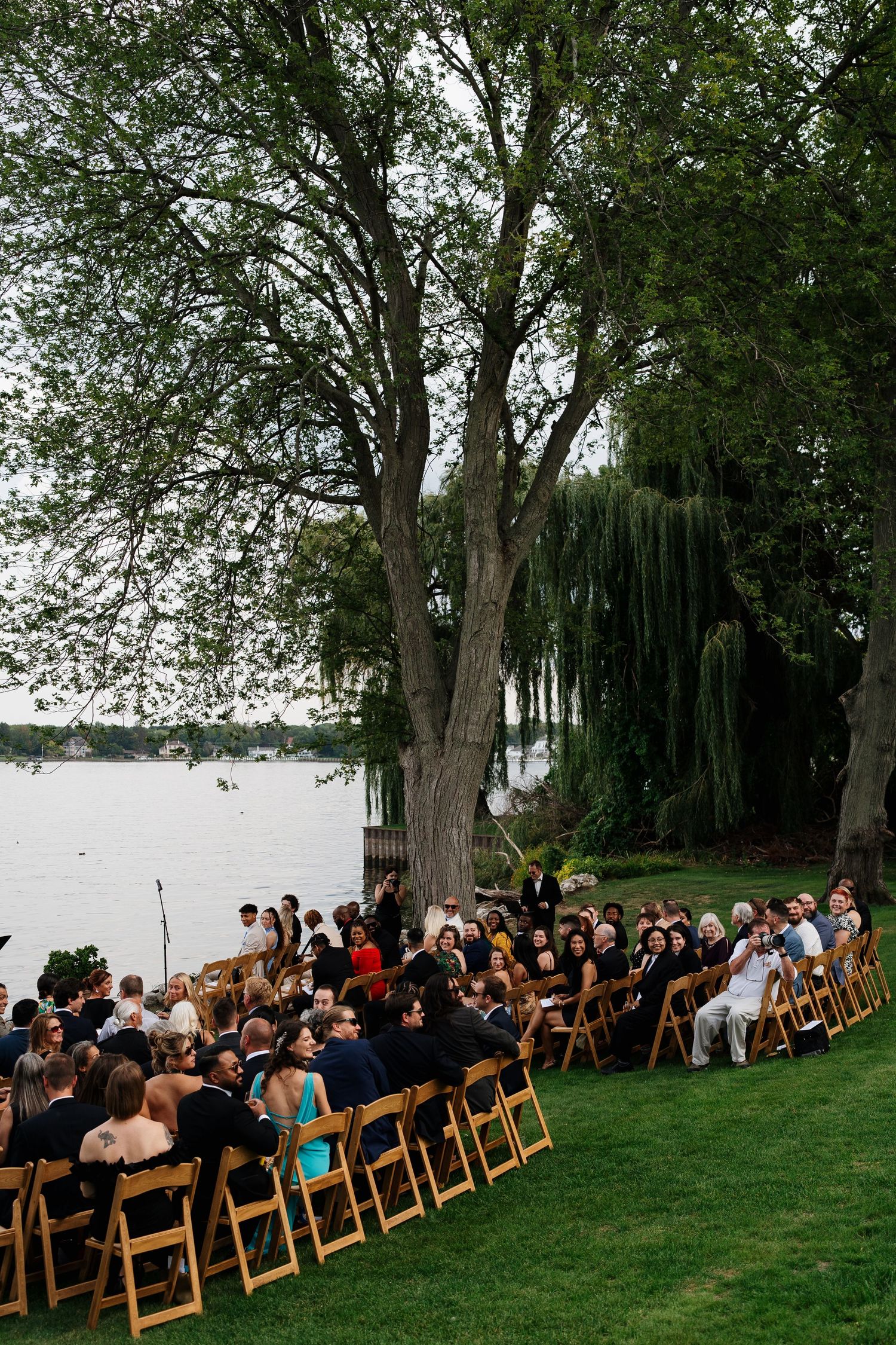 Guests seated beneath a large tree for an outdoor Lake Michigan wedding ceremony in Holland, Michigan.