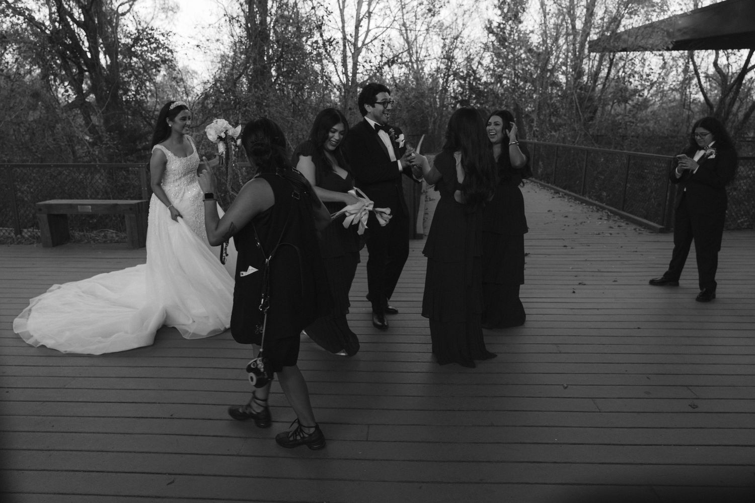 Wedding party gathered on outdoor deck celebrating with bride in white gown and guests in black attire.