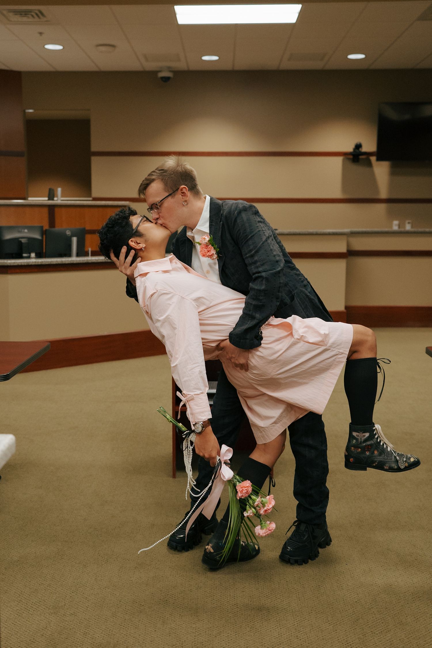 Newlyweds sharing romantic dip kiss after courthouse wedding ceremony with bouquet in hand.