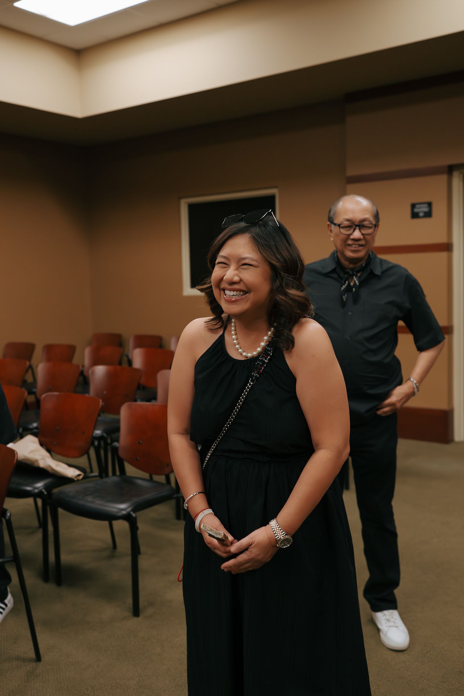 Joyful Asian woman in black dress smiling at intimate courthouse wedding celebration.