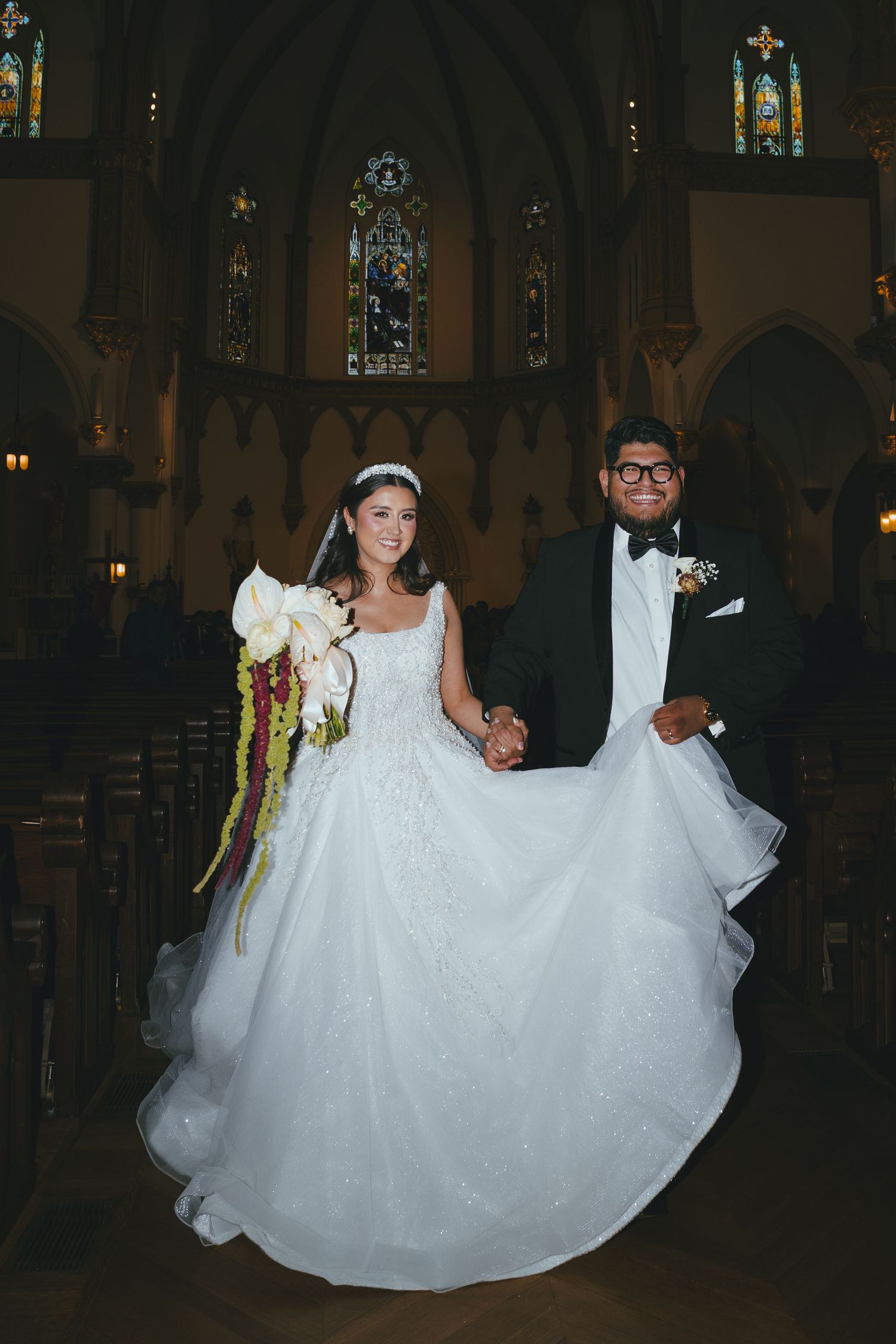 Newlyweds smile and hold hands walking down the church aisle after their wedding ceremony.