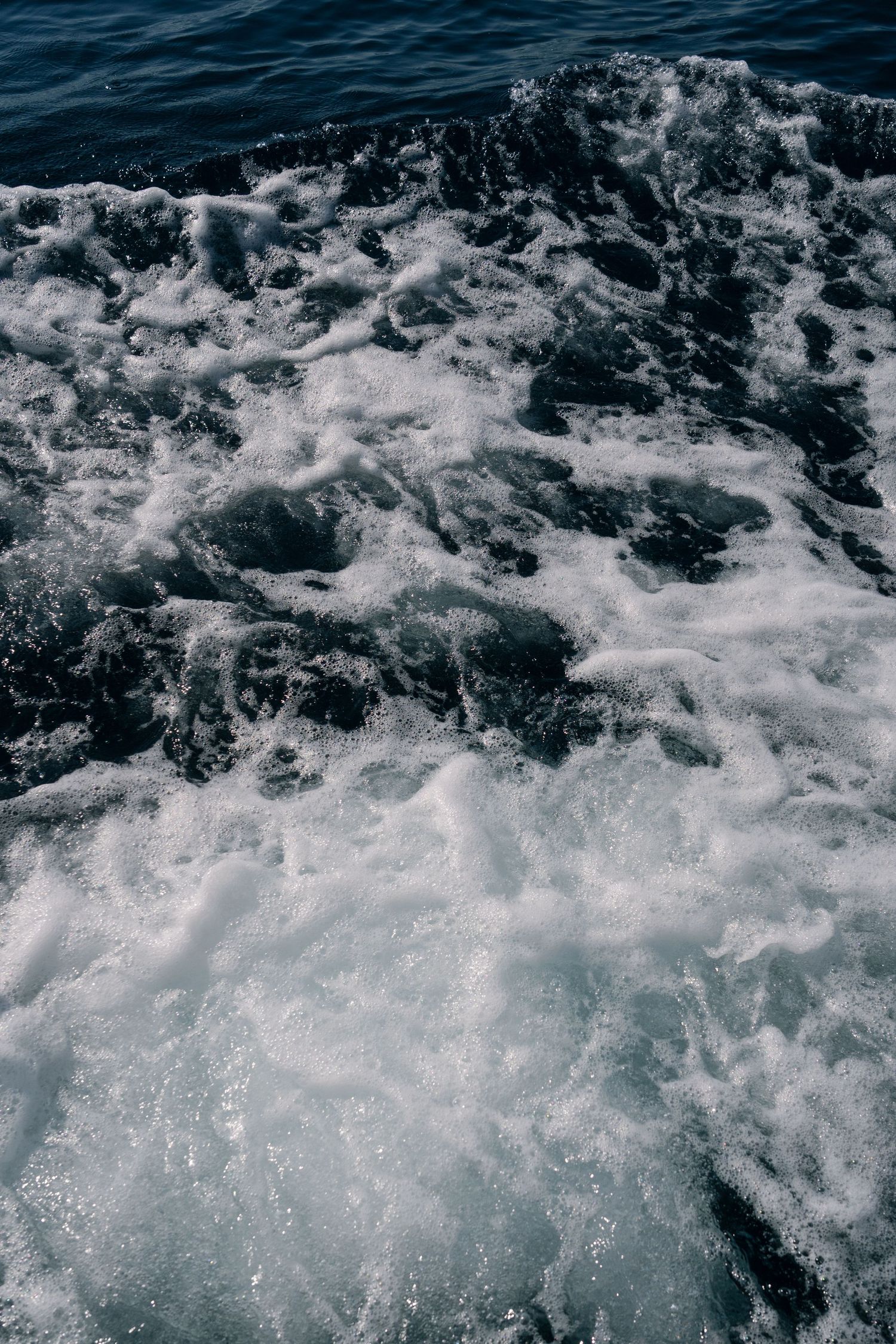Turbulent ocean waves with white sea foam and frothy water surface, dark blue sea in the background.