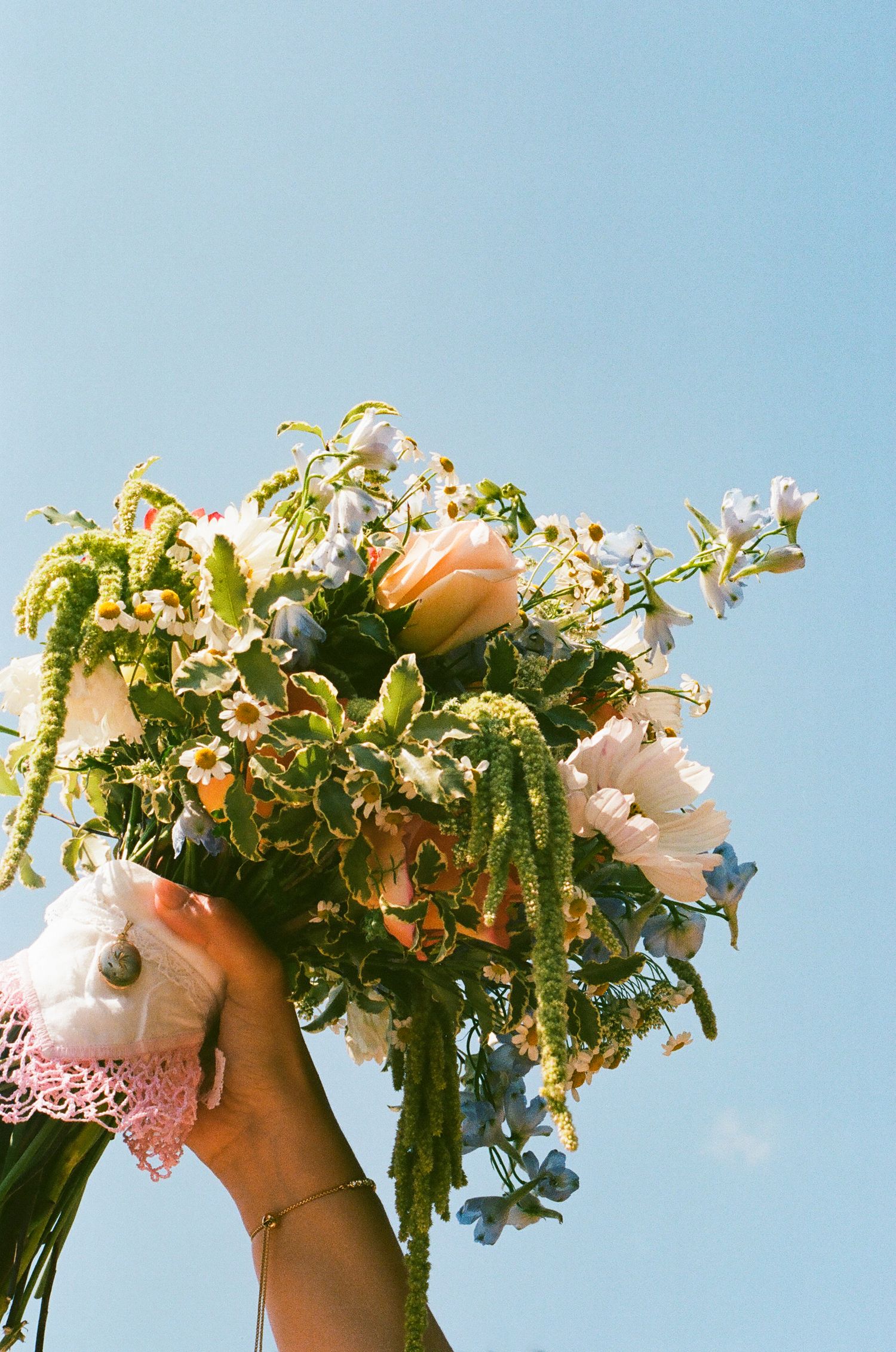 Bride holding her wedding bouquet beneath a clear blue sky.