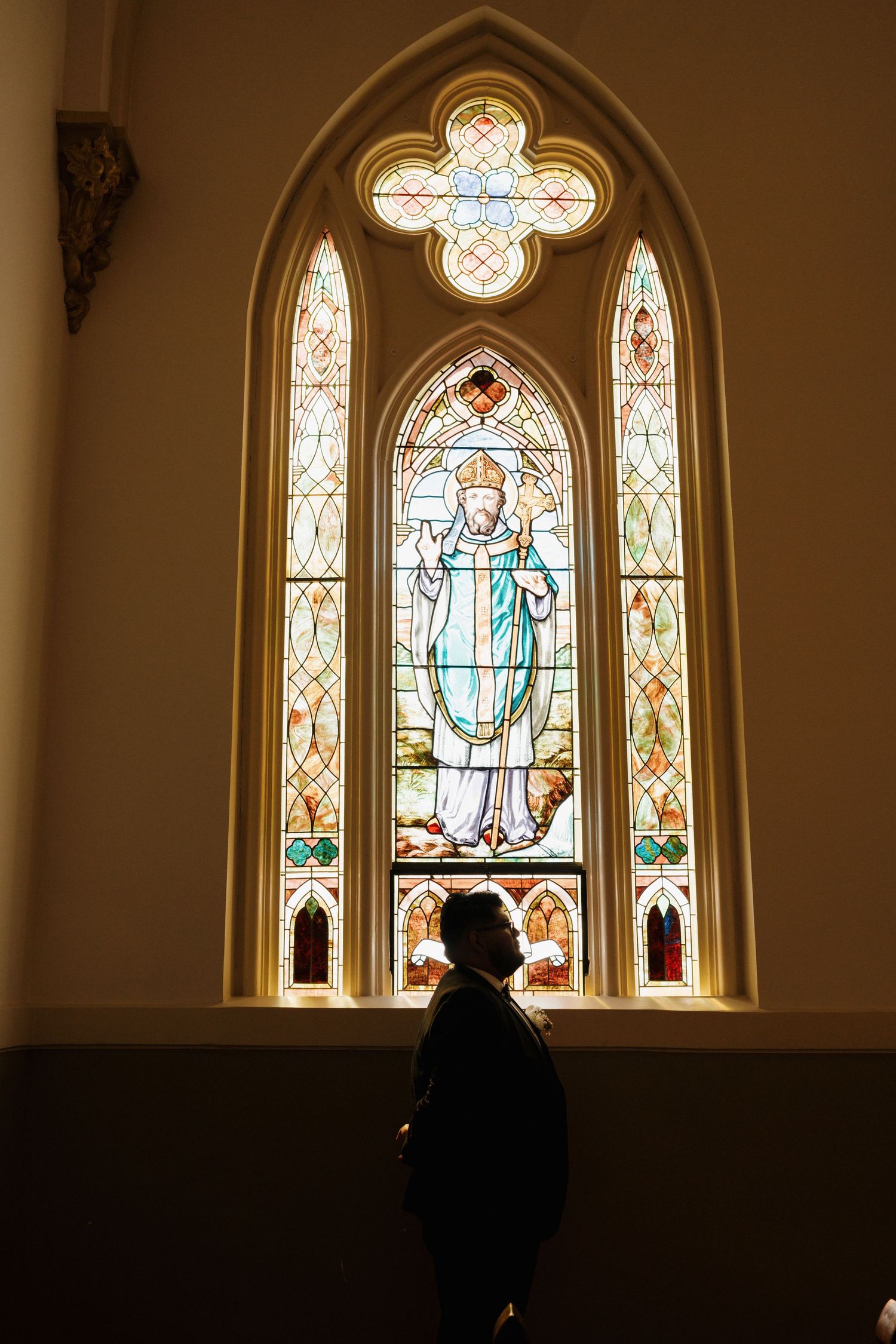 Silhouette of a person standing before a stunning stained glass church window depicting a saint.