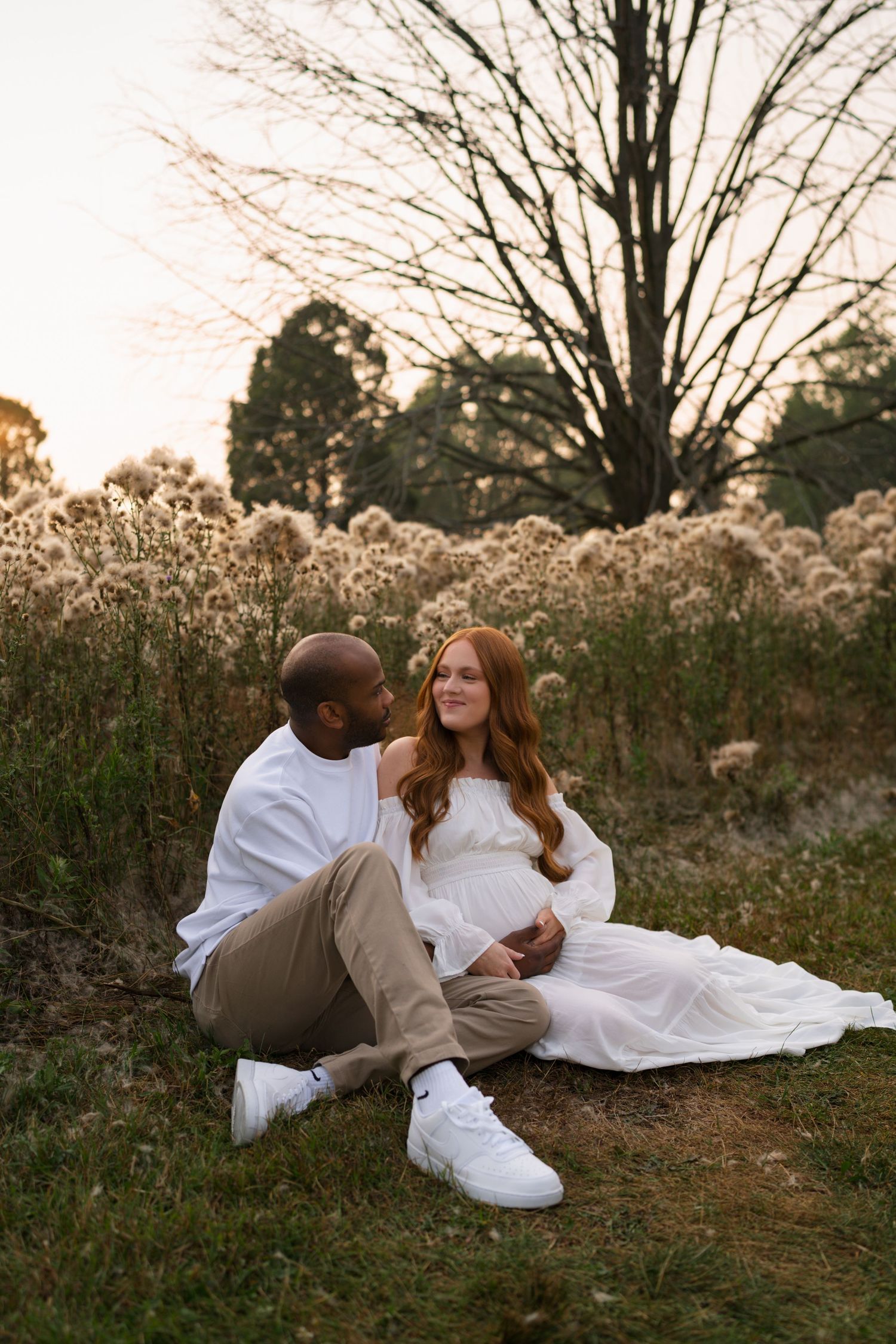 Expectant parents embracing while seated in the tall grasses at Highlands Prairie.