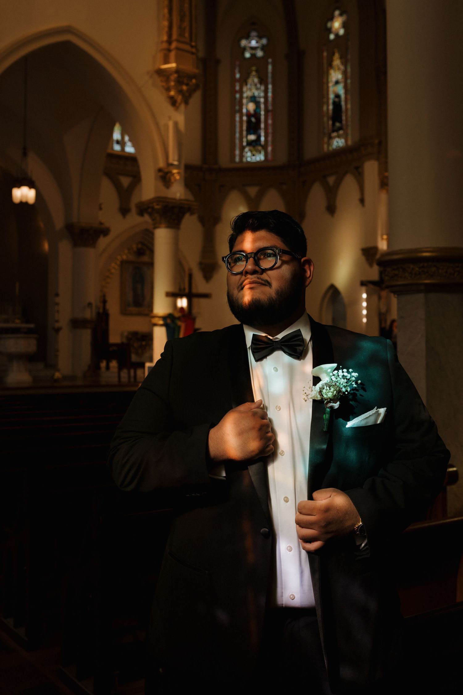 Groom in black tuxedo adjusting jacket lapel inside a warmly lit Gothic cathedral.