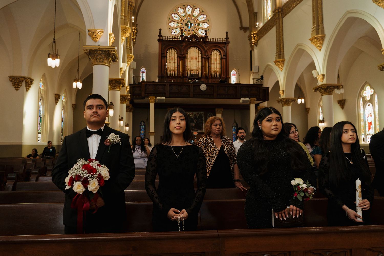 Guests in formal attire standing in a decorated Catholic church during a wedding ceremony.