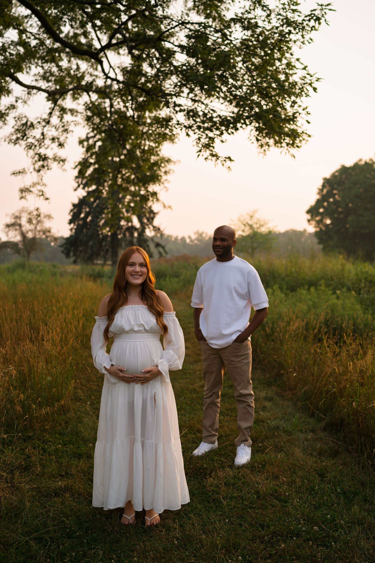 Expectant mother holding her baby bump while standing in tall prairie grasses.
