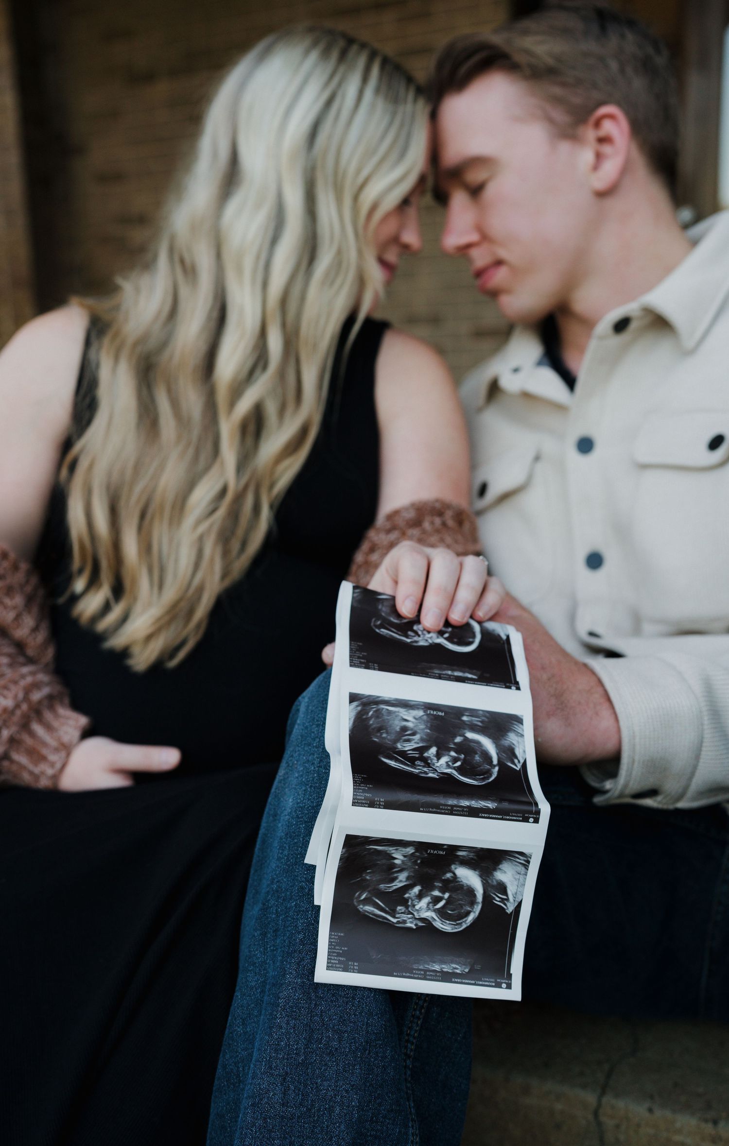 Close-up of couple touching foreheads while holding ultrasound photos, announcing pregnancy.