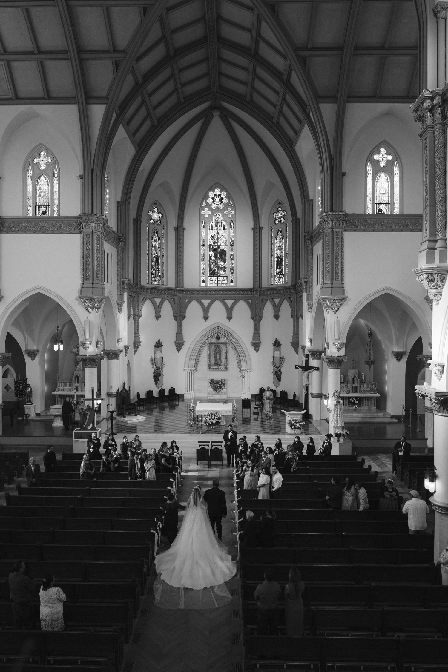 Black and white aerial view of a bride walking down the aisle of an ornate Gothic cathedral.