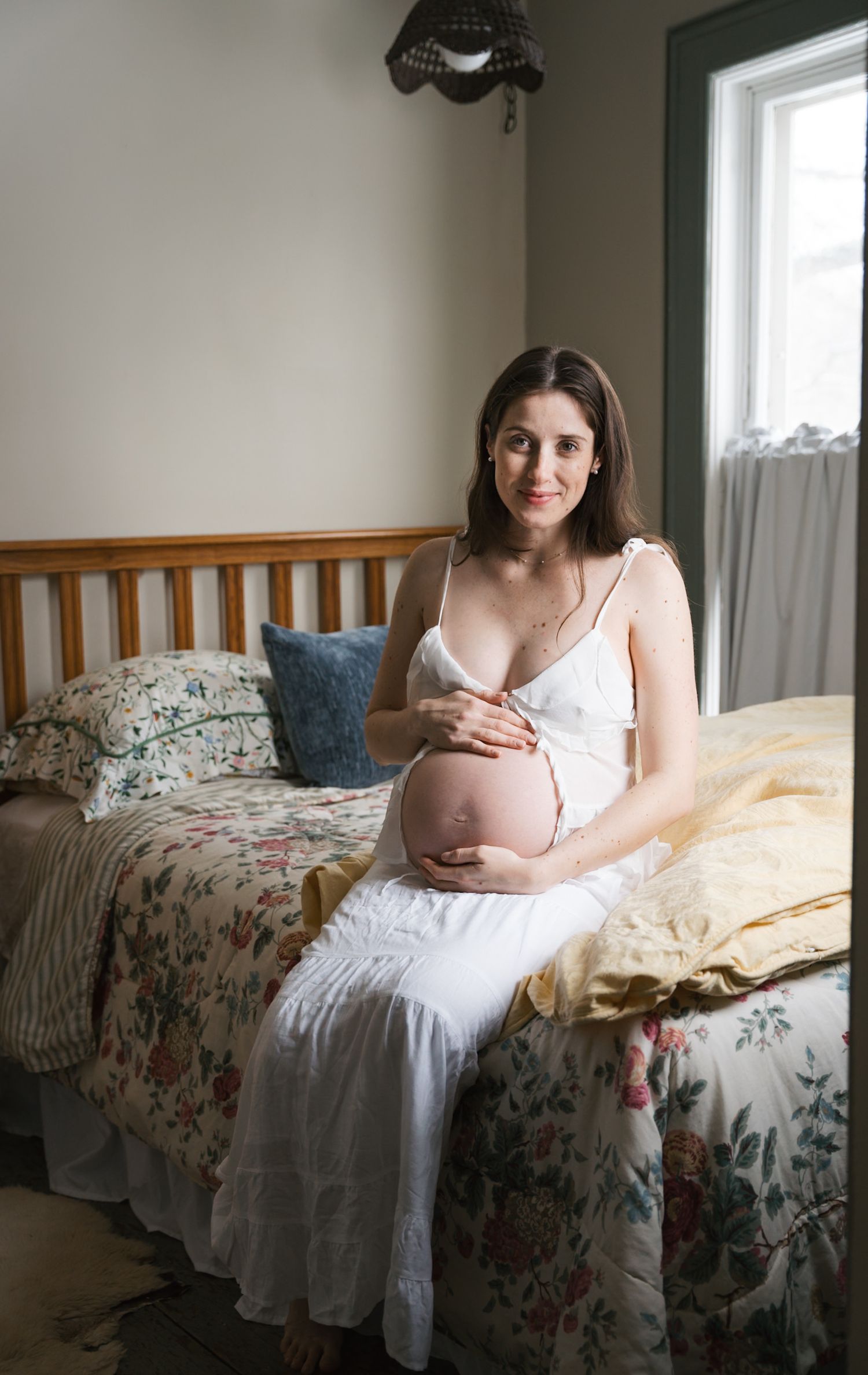 Expectant mother sitting peacefully on a bed during an in-home maternity session.
