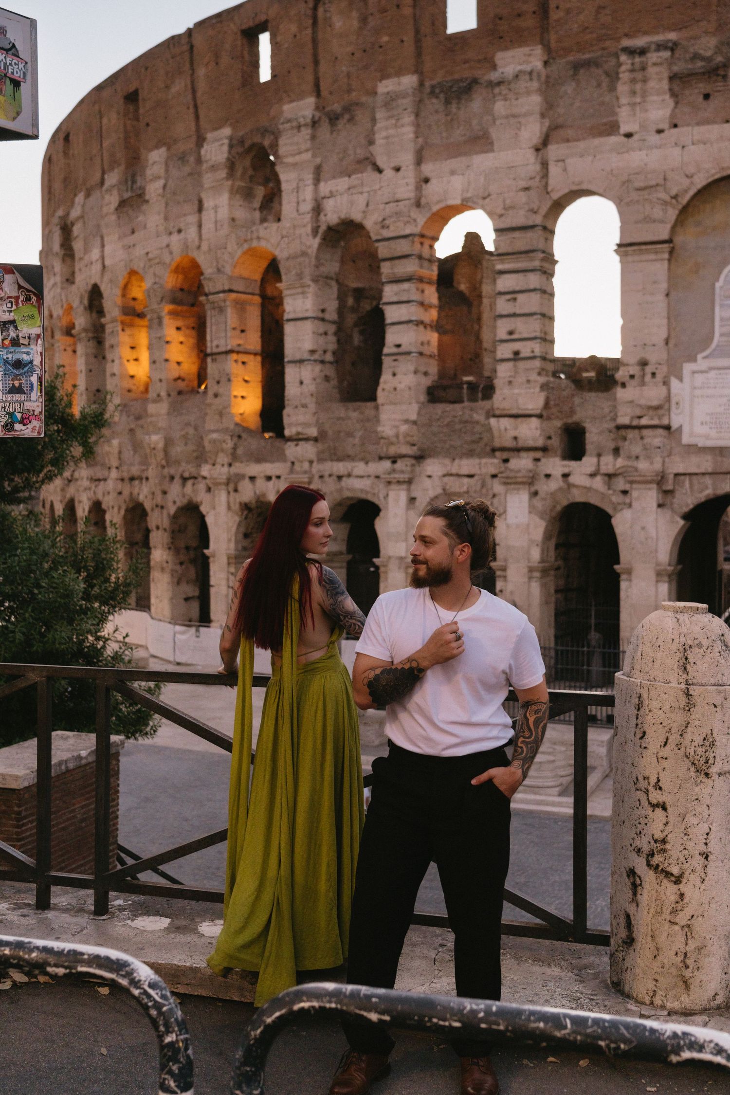 Couple posing romantically in front of the illuminated Colosseum in Rome, woman in green dress, man in white shirt.