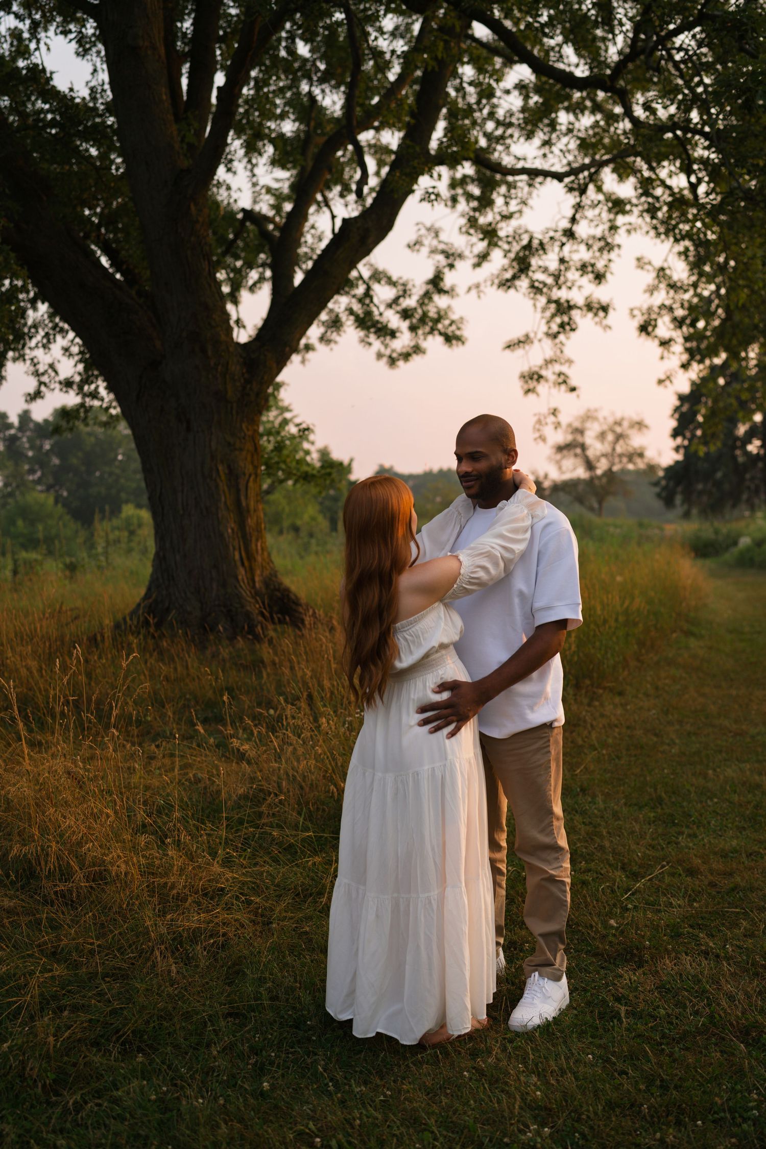 Expectant mother smiling softly while standing in the prairie.