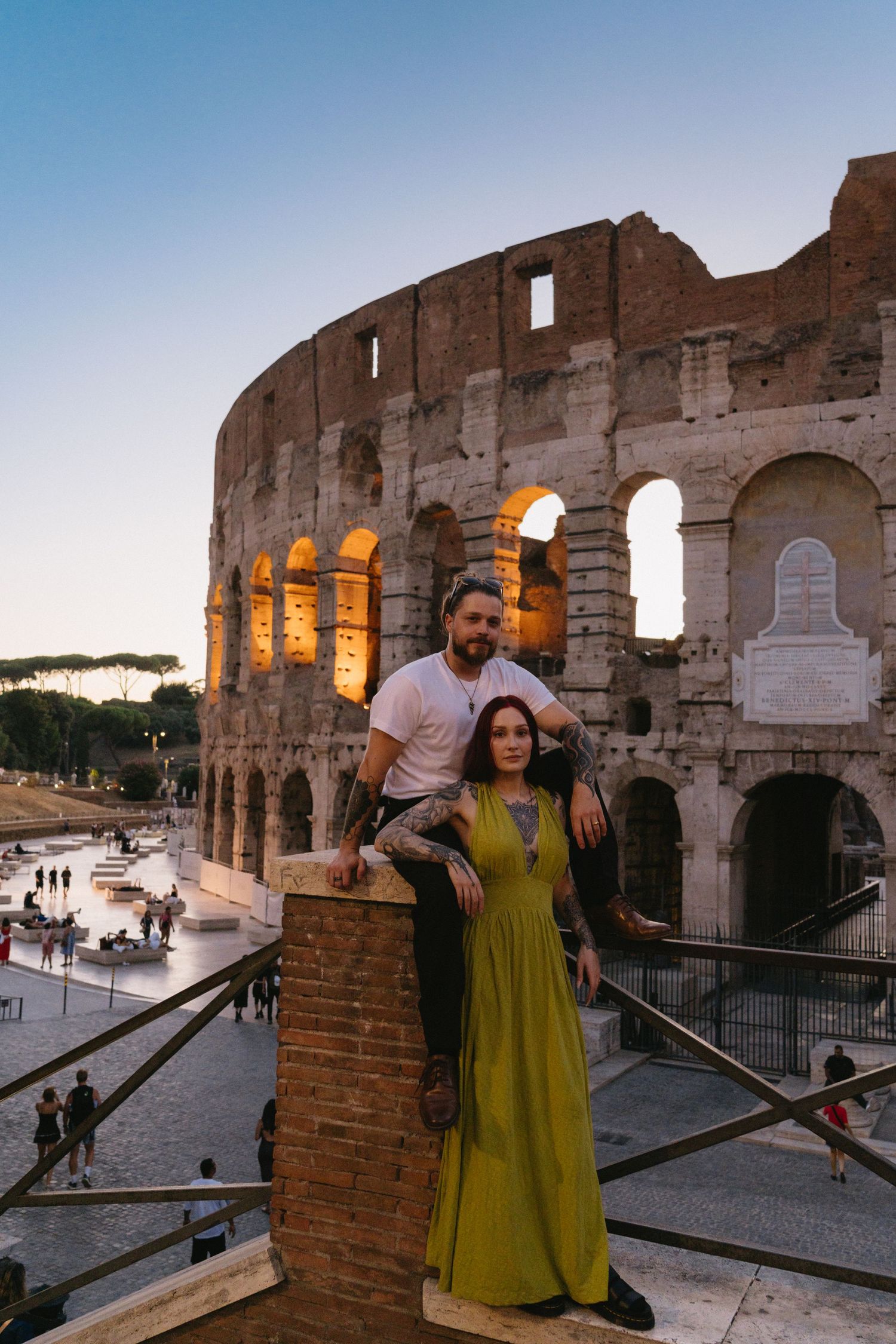 Couple posing in front of the illuminated Colosseum in Rome at dusk, woman in green dress.