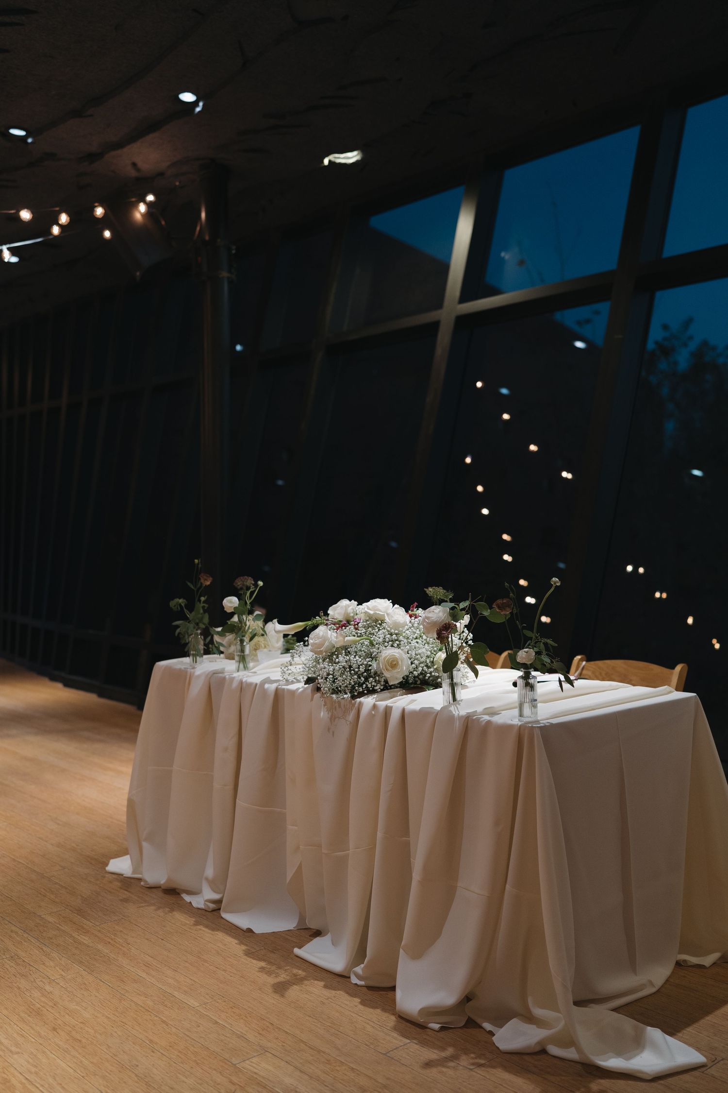 Elegant wedding sweetheart table with white linen and floral centerpiece in dimly lit venue.