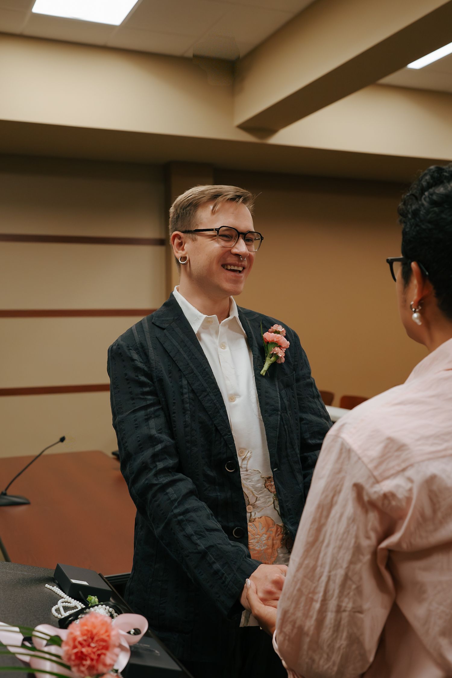 Smiling groom in dark blazer with boutonniere exchanging vows at courthouse wedding ceremony.
