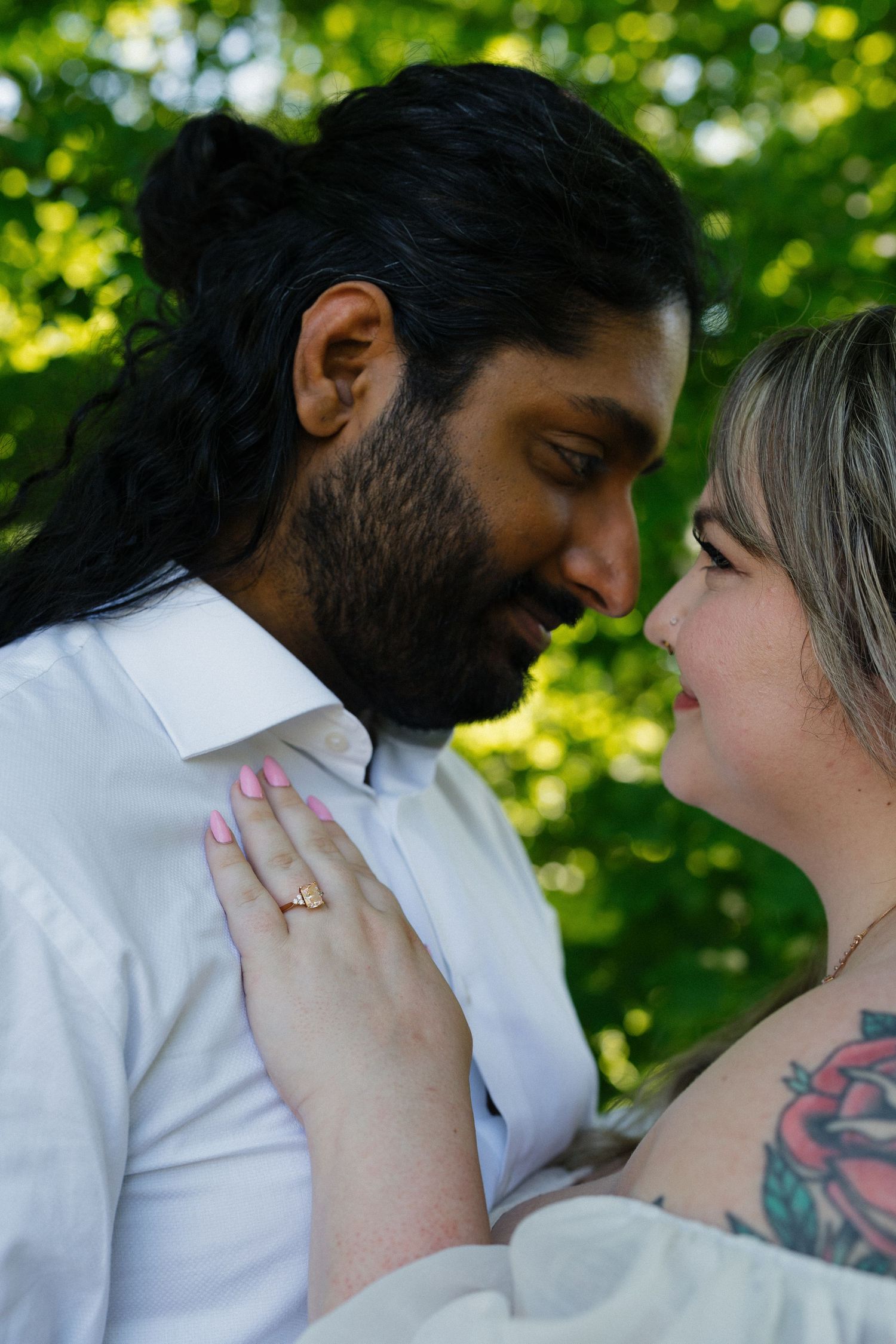 Close-up of interracial couple leaning in for a kiss outdoors with lush green foliage background.