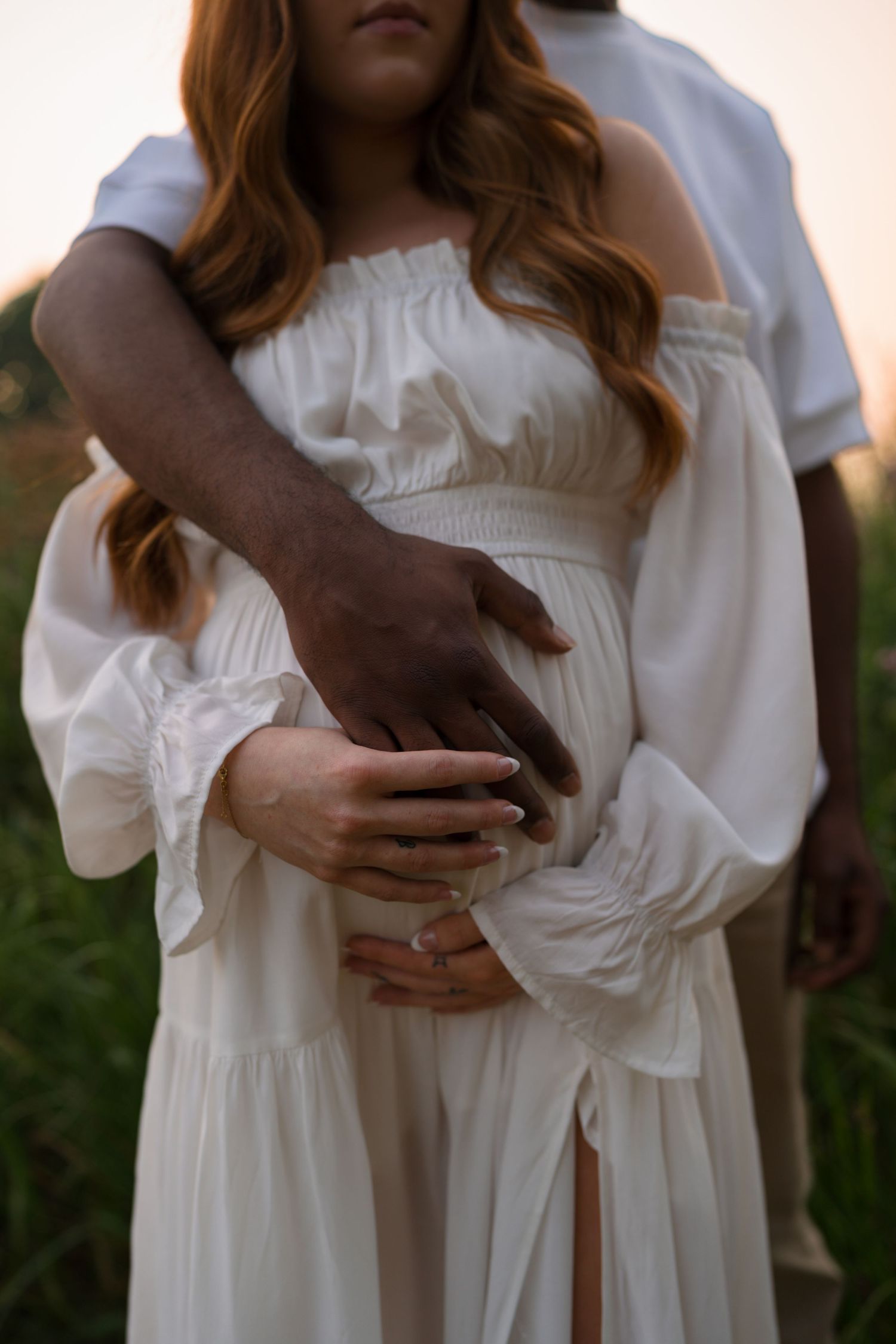 Expectant parents standing close together in the golden prairie at Highlands Prairie.