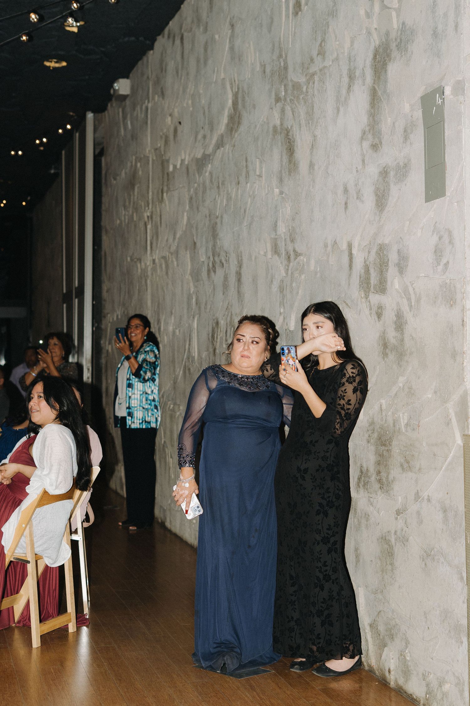 Two women in formal gowns using smartphones to capture moments at a wedding reception.