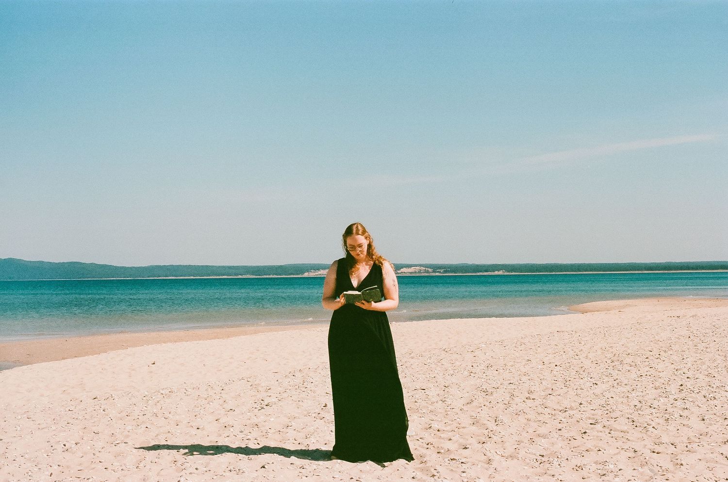 Woman in black maxi dress standing on a white sand beach by turquoise water.