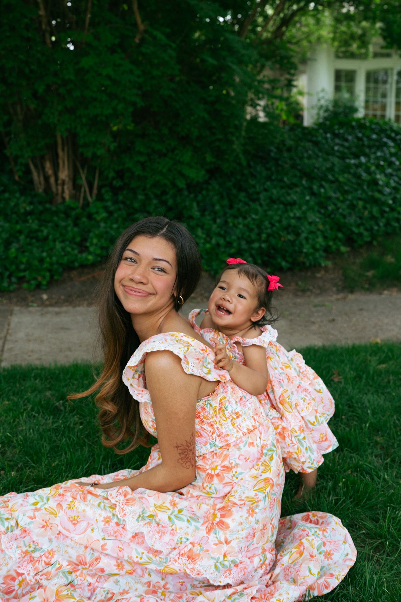 Photographer Mariah Rosalinda smiling at a mother and daughter share a joyful moment in the background. Daughter embraces mother very happy.