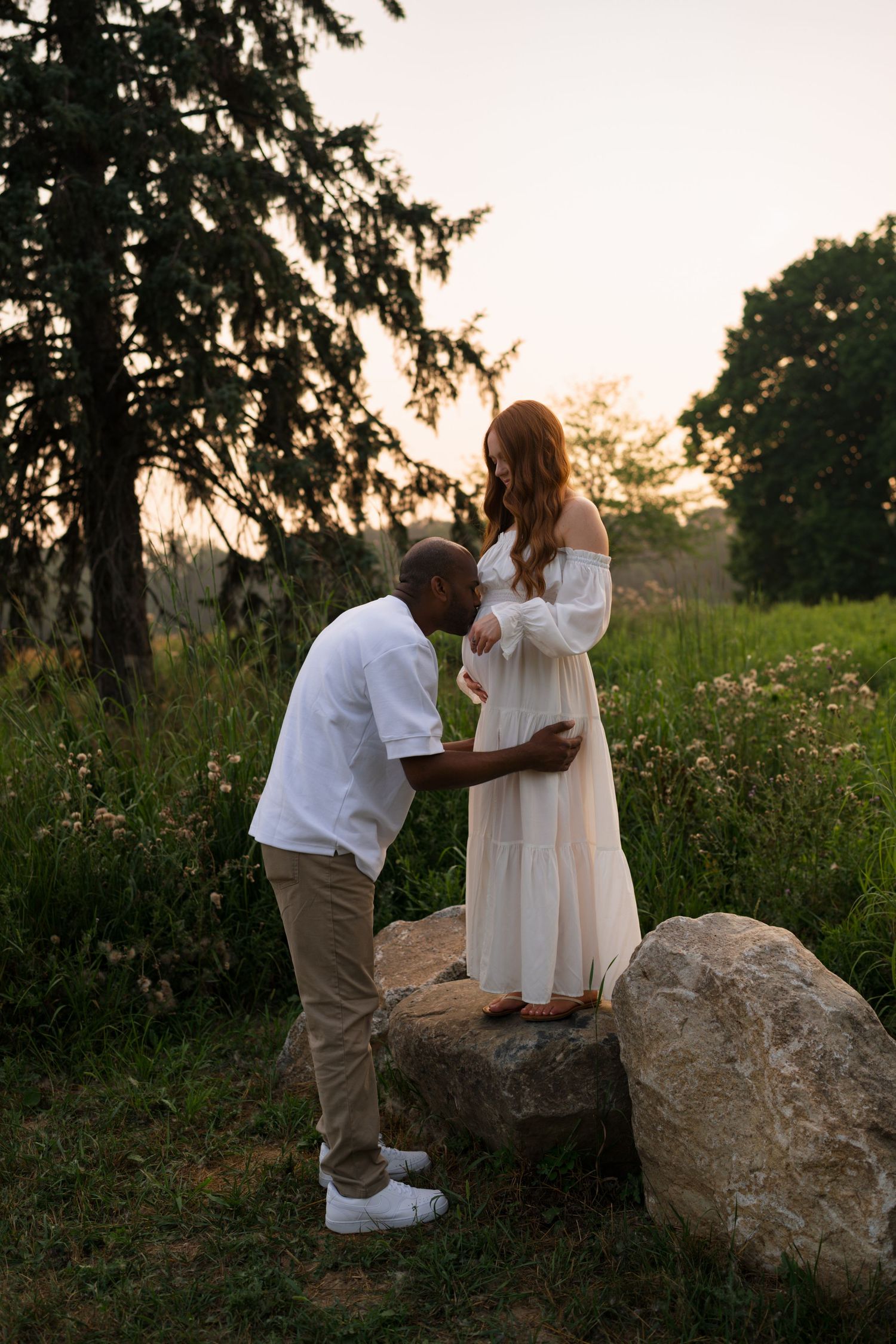 Expectant parents embracing in the tall grasses at Highlands Prairie.