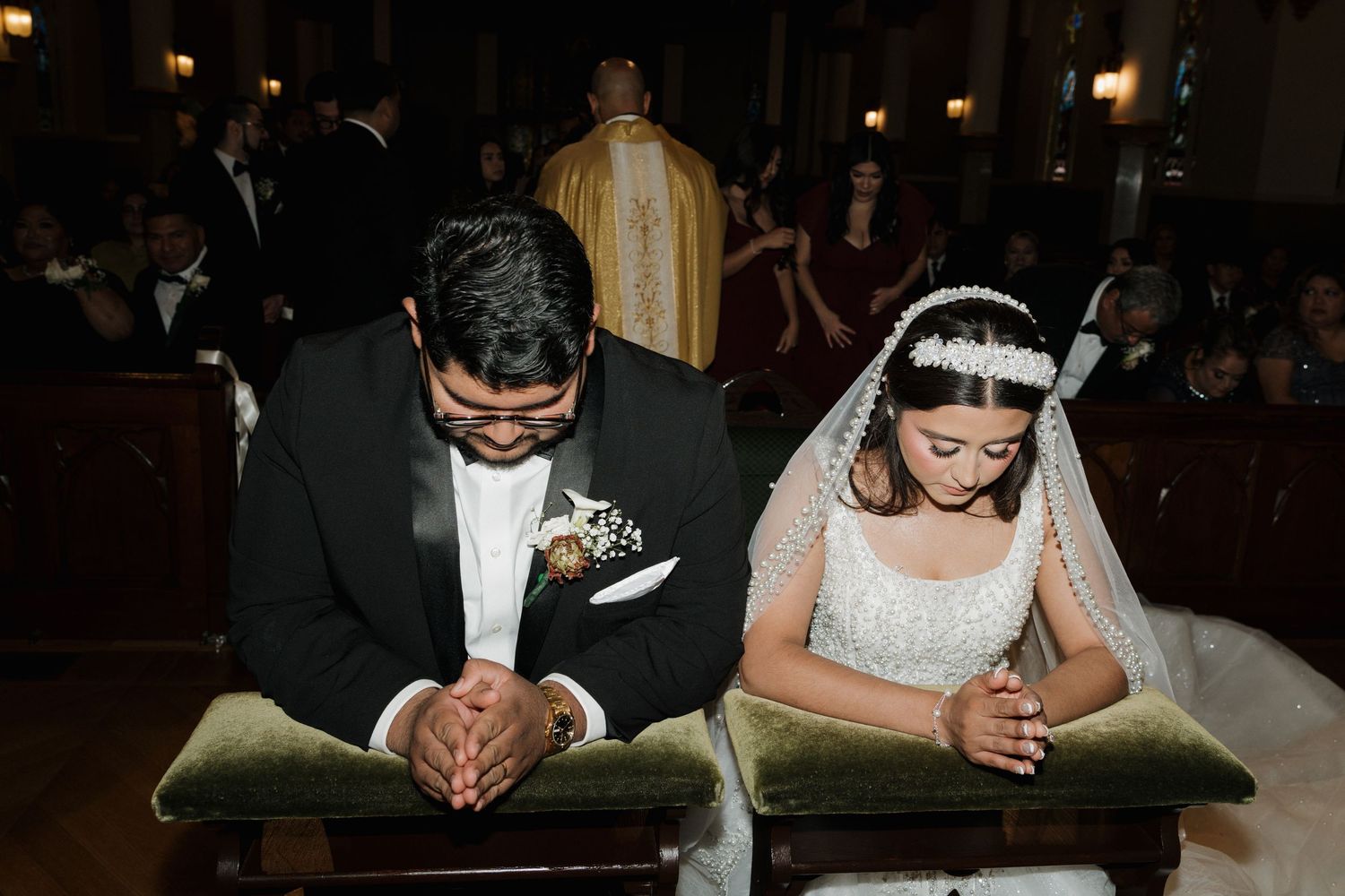 Bride and groom kneel in prayer at the altar during their traditional Catholic wedding ceremony.