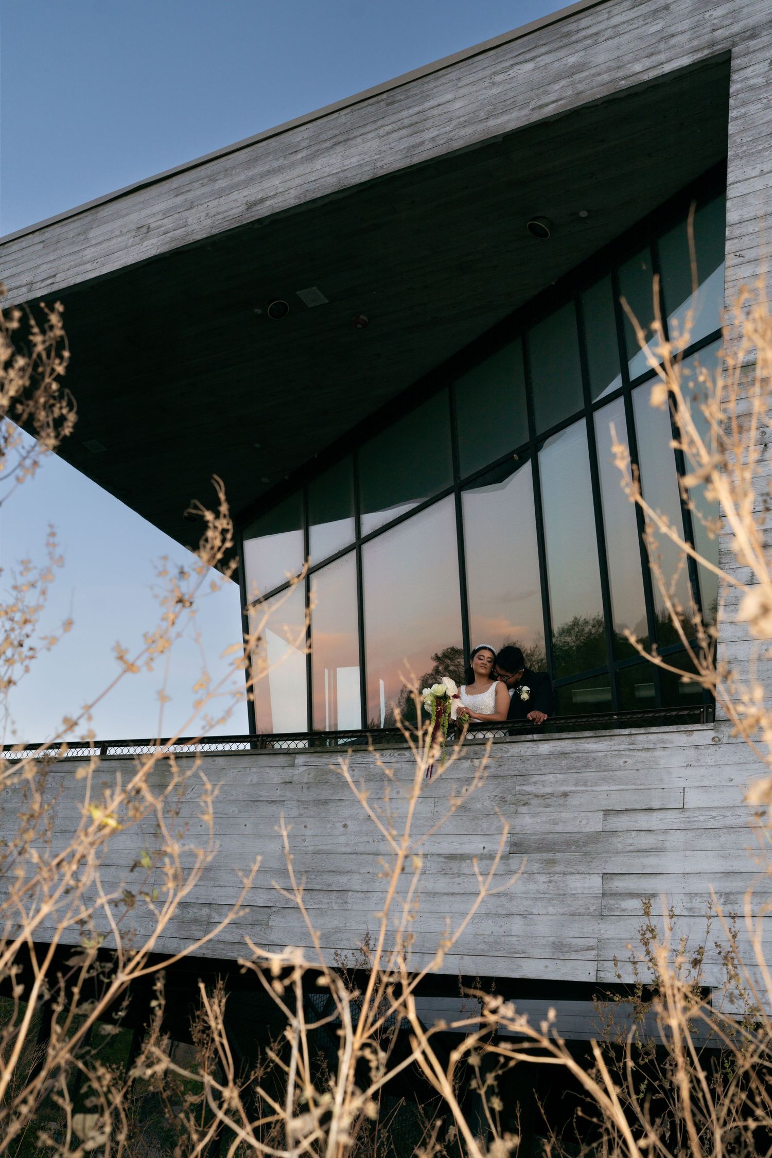 Bride and groom sharing intimate moment on rustic wooden balcony at golden hour sunset.