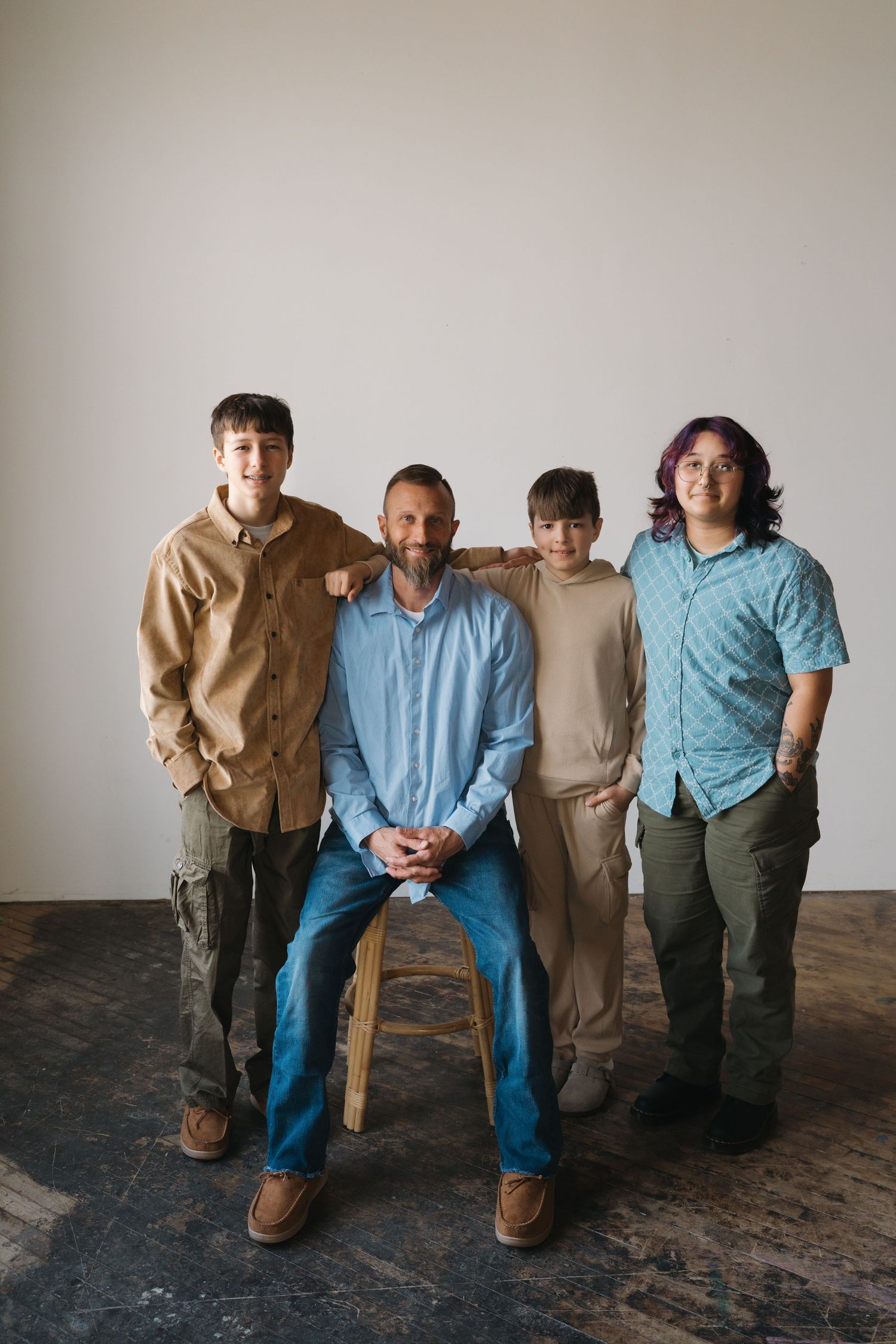 Father sitting on stool with three sons standing beside him in a bright white studio setting.