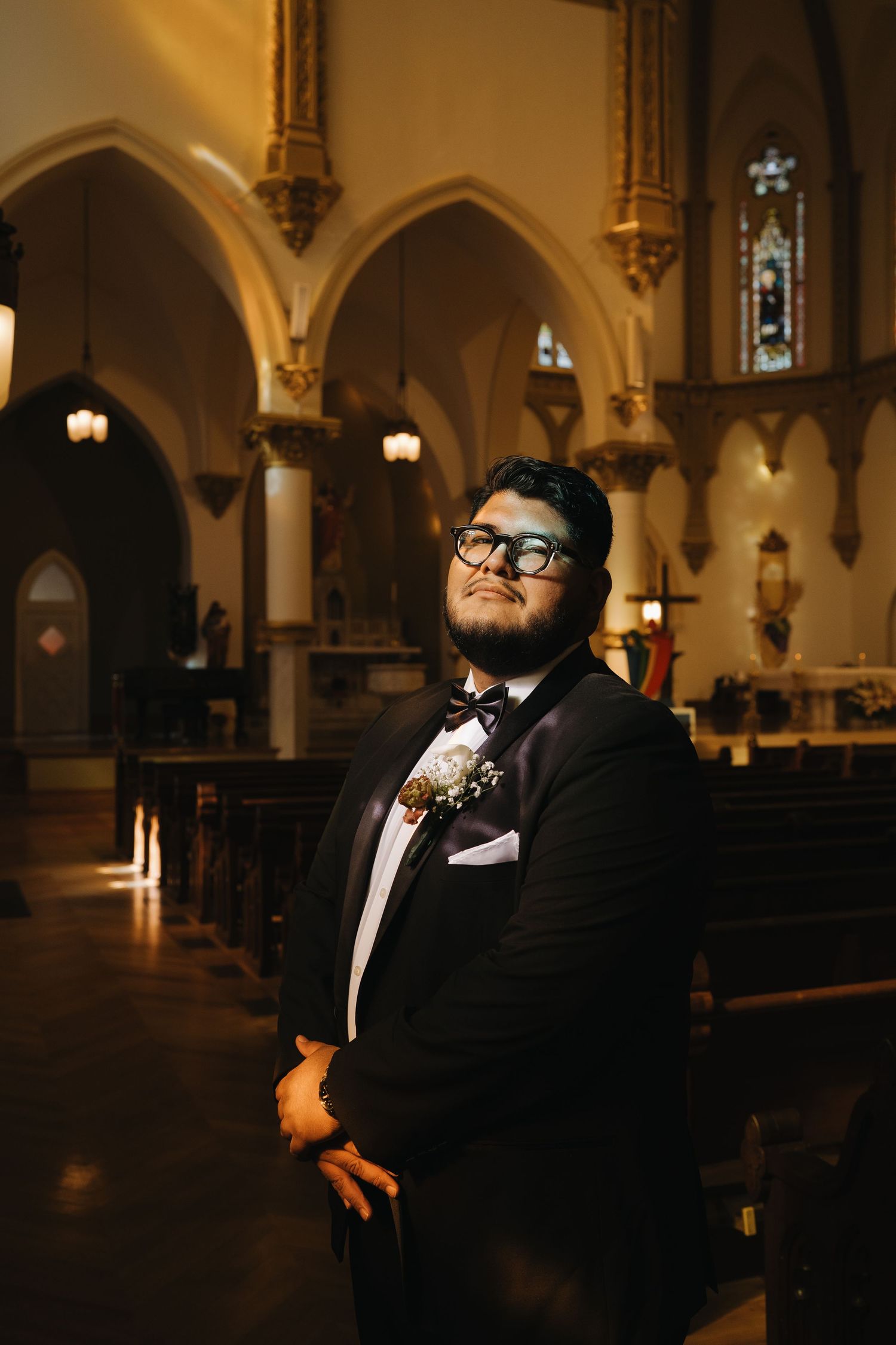 Dapper groom in black tuxedo with boutonniere posing inside an ornate Gothic-style church.