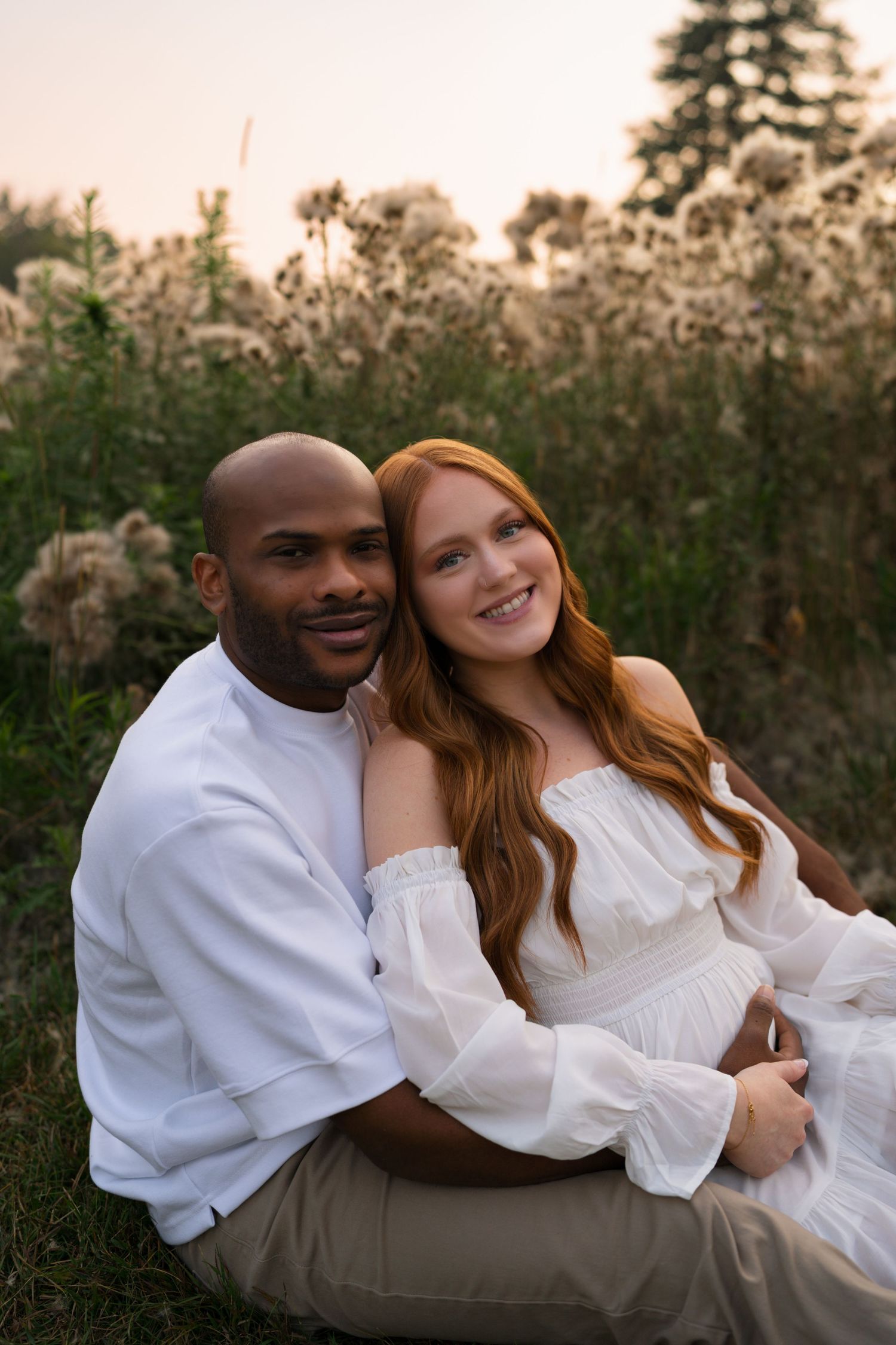 Expectant parents sitting together in the prairie during a golden hour maternity session.