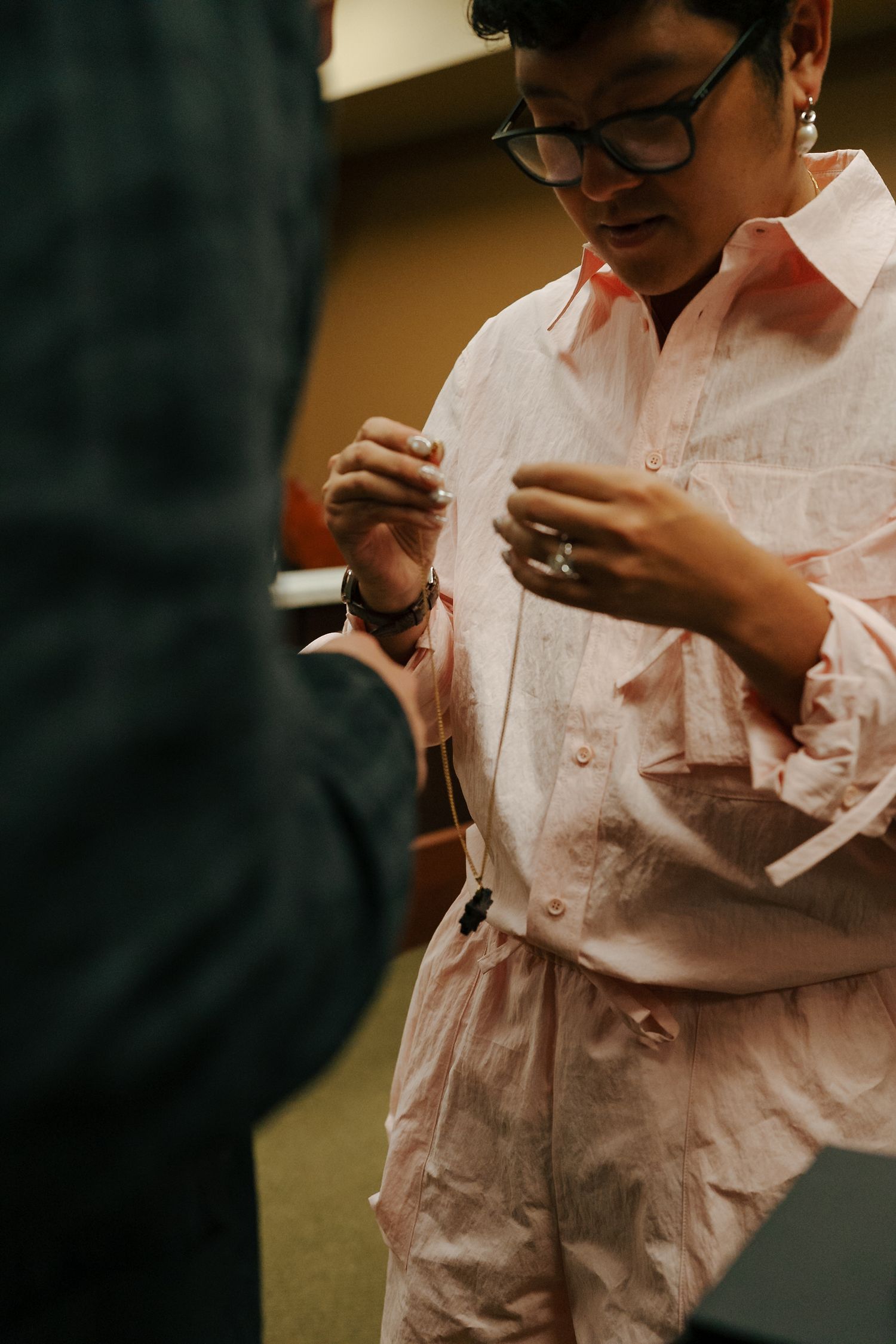 Person in pink outfit fastening a necklace during intimate courthouse wedding exchange.