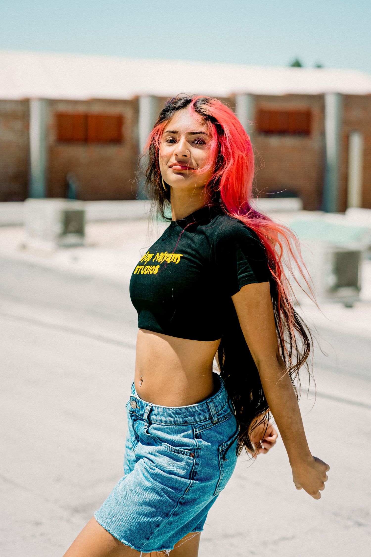 Young woman with vibrant red and black hair wearing a crop top and denim skirt posing outdoors.