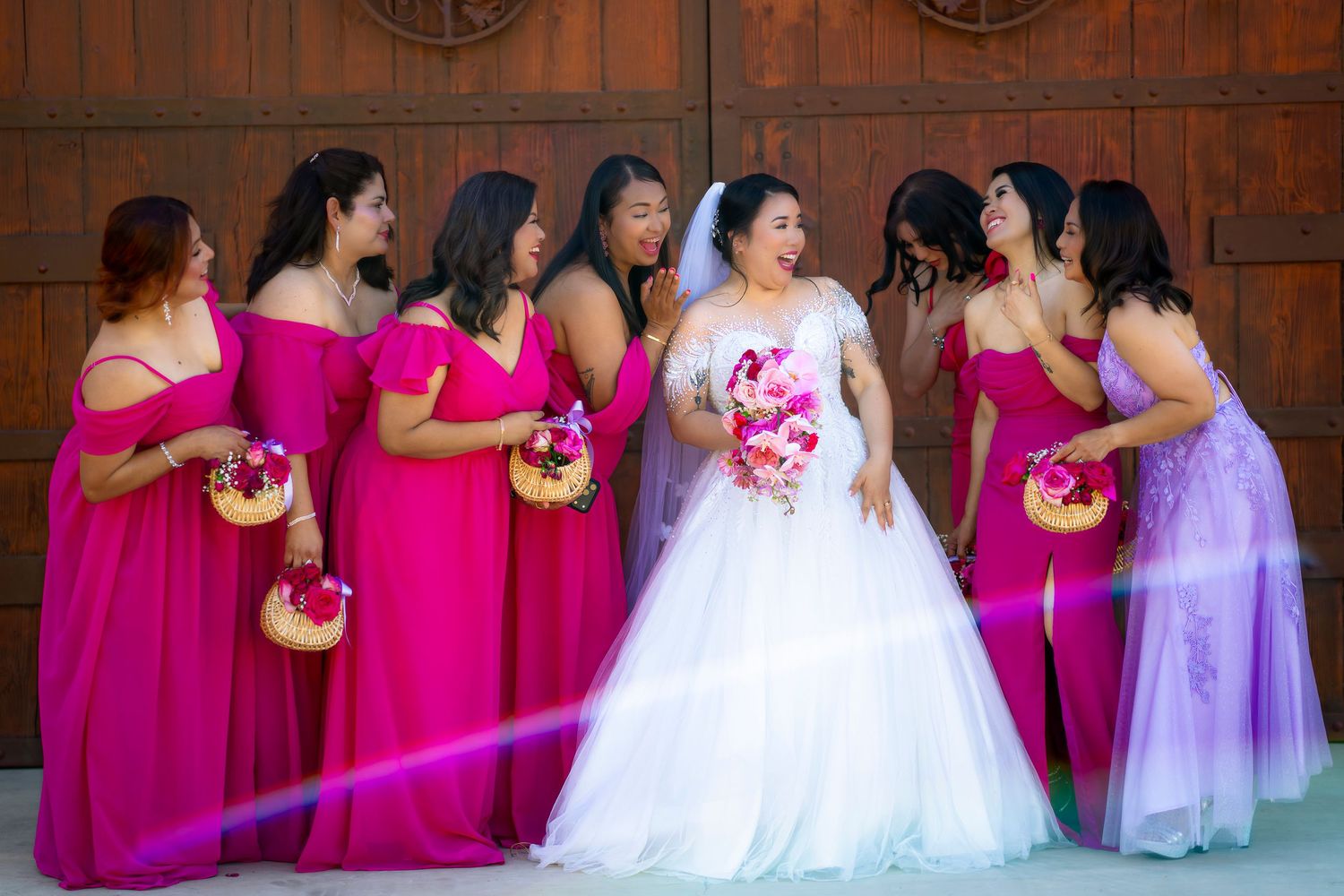 Bride in white gown with bridesmaids in pink dresses holding bouquets at church.