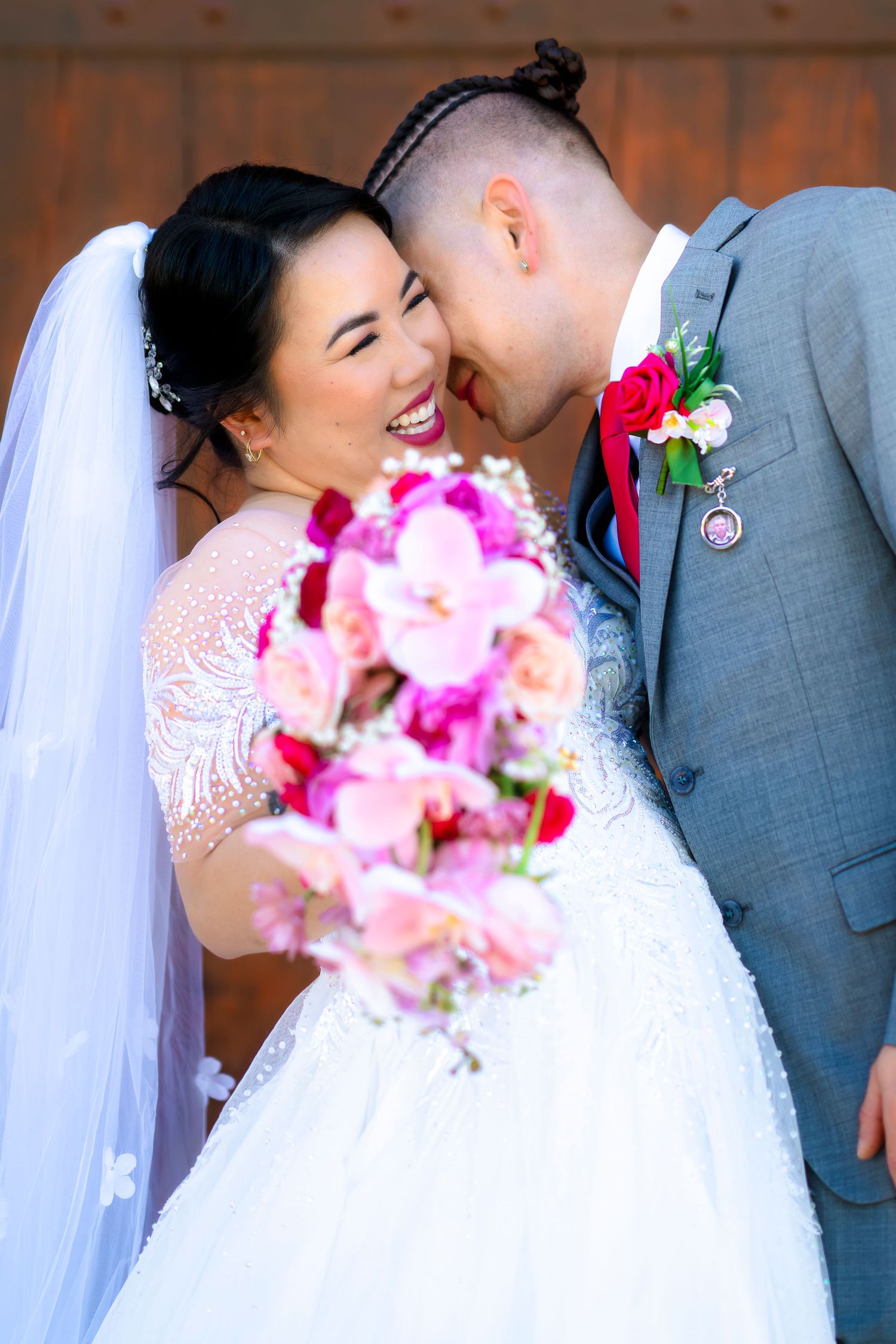 Laughing bride and groom touching foreheads with cascading pink orchid bouquet.